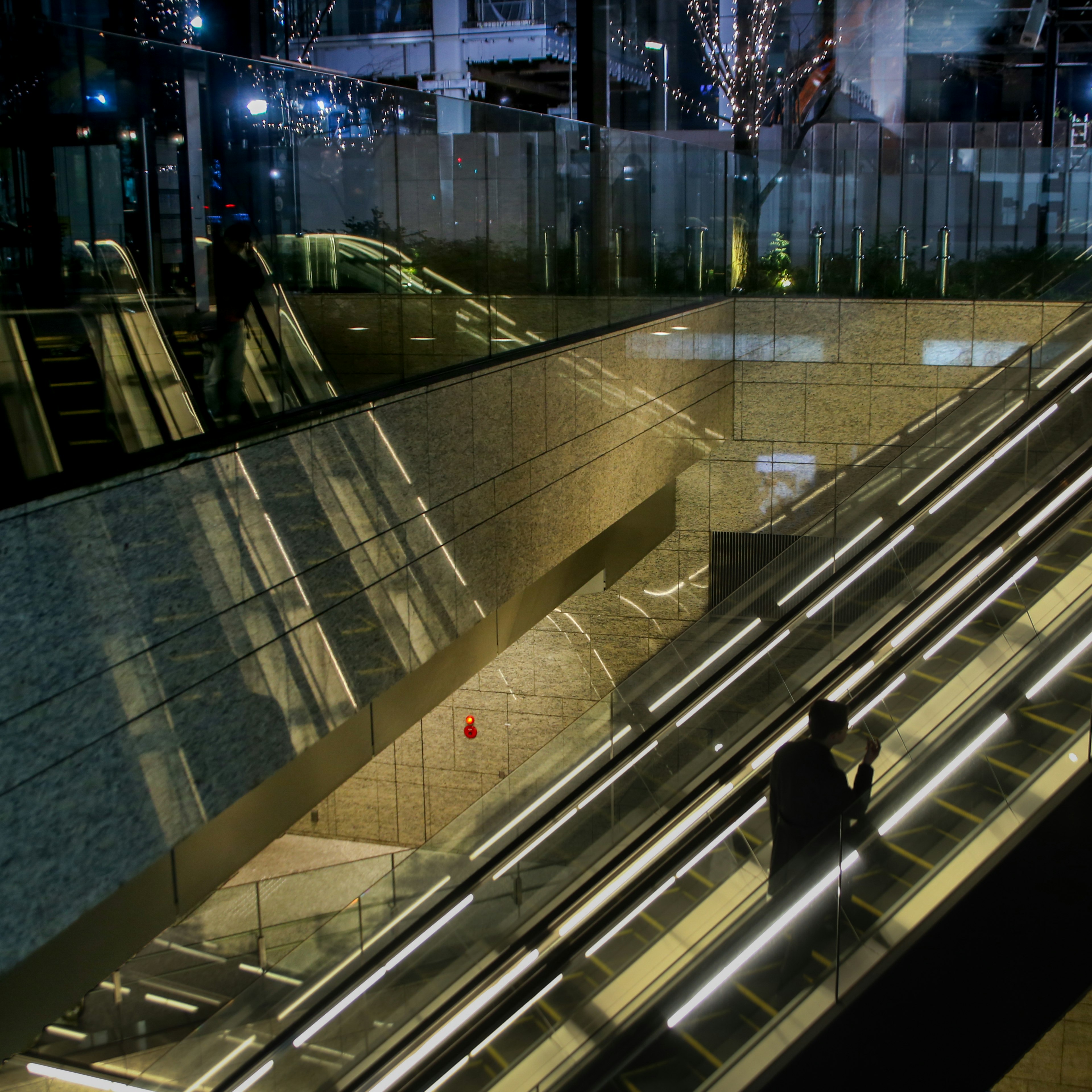 Interior de un edificio moderno con escalera mecánica iluminada por la noche que muestra reflejos y efectos de luz