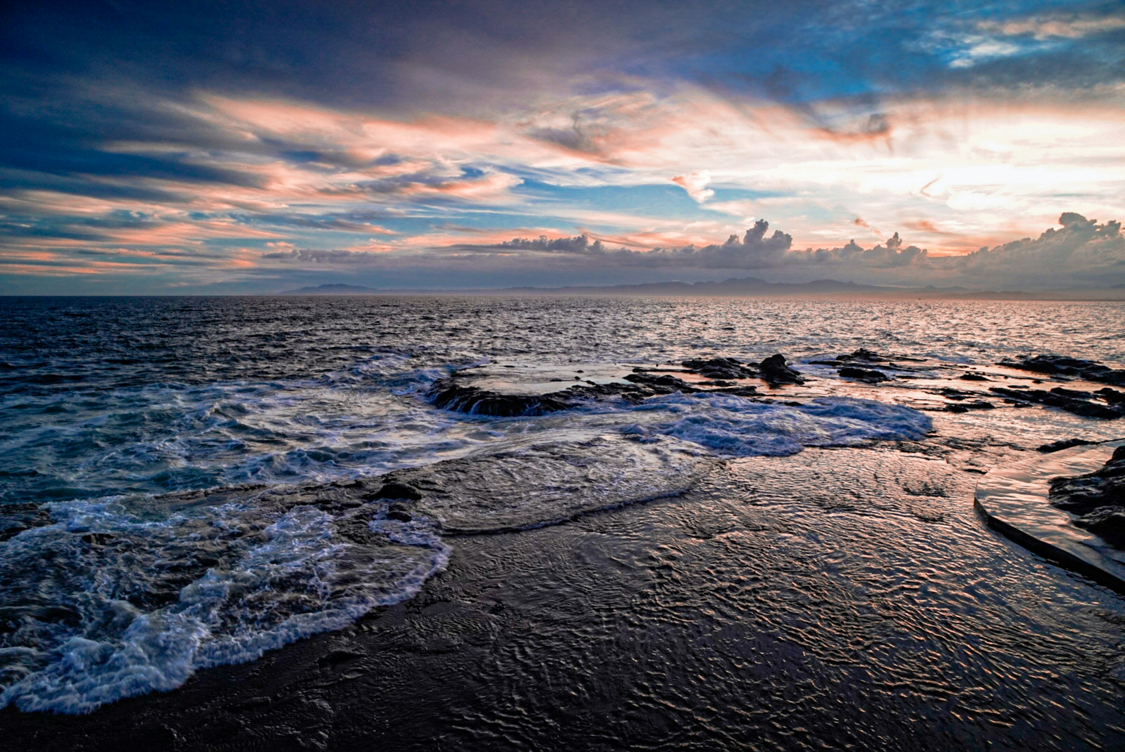 Pemandangan laut saat matahari terbenam dengan pantai berbatu