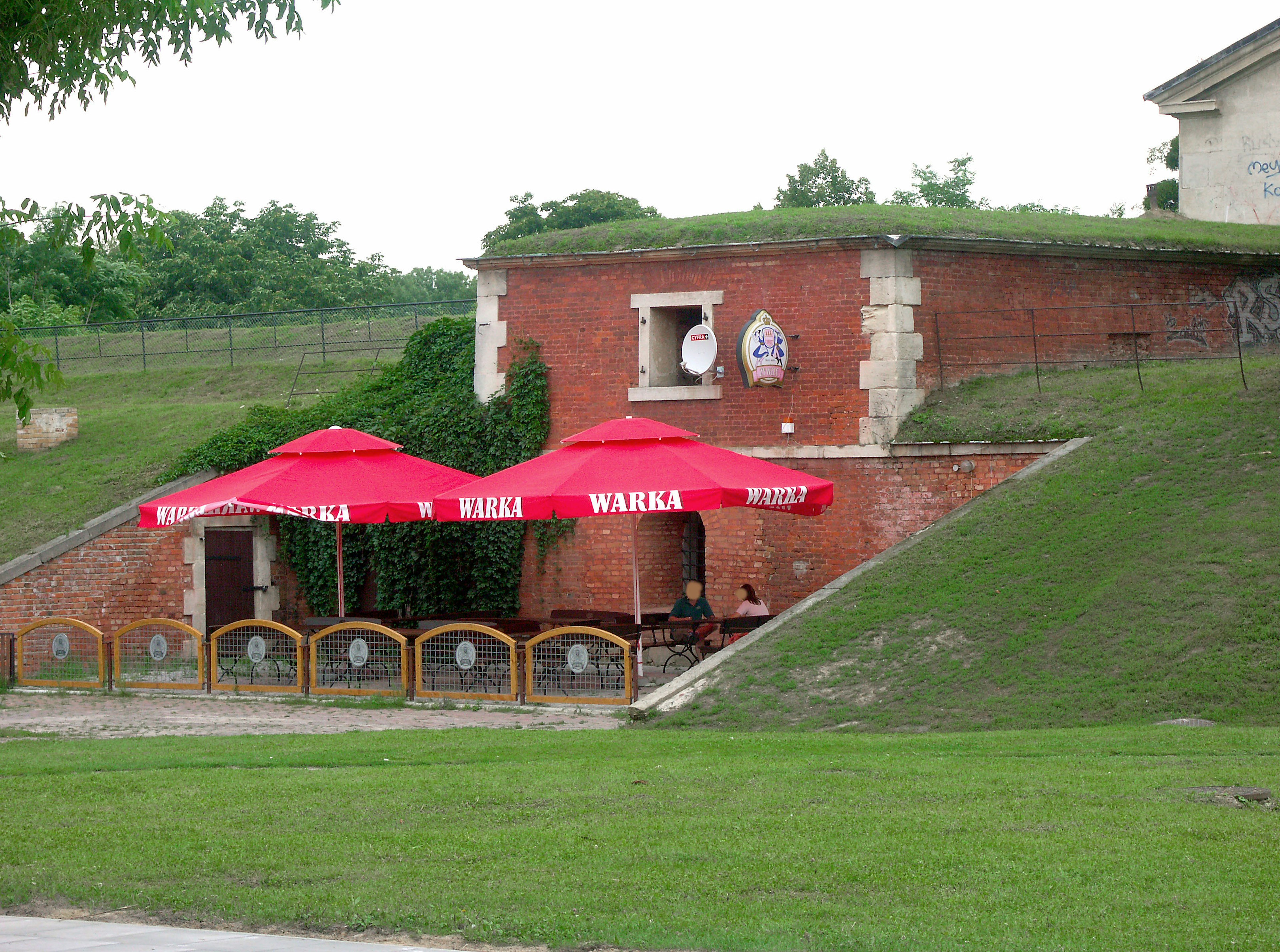 Eksterior restoran dengan payung merah dan bukit hijau