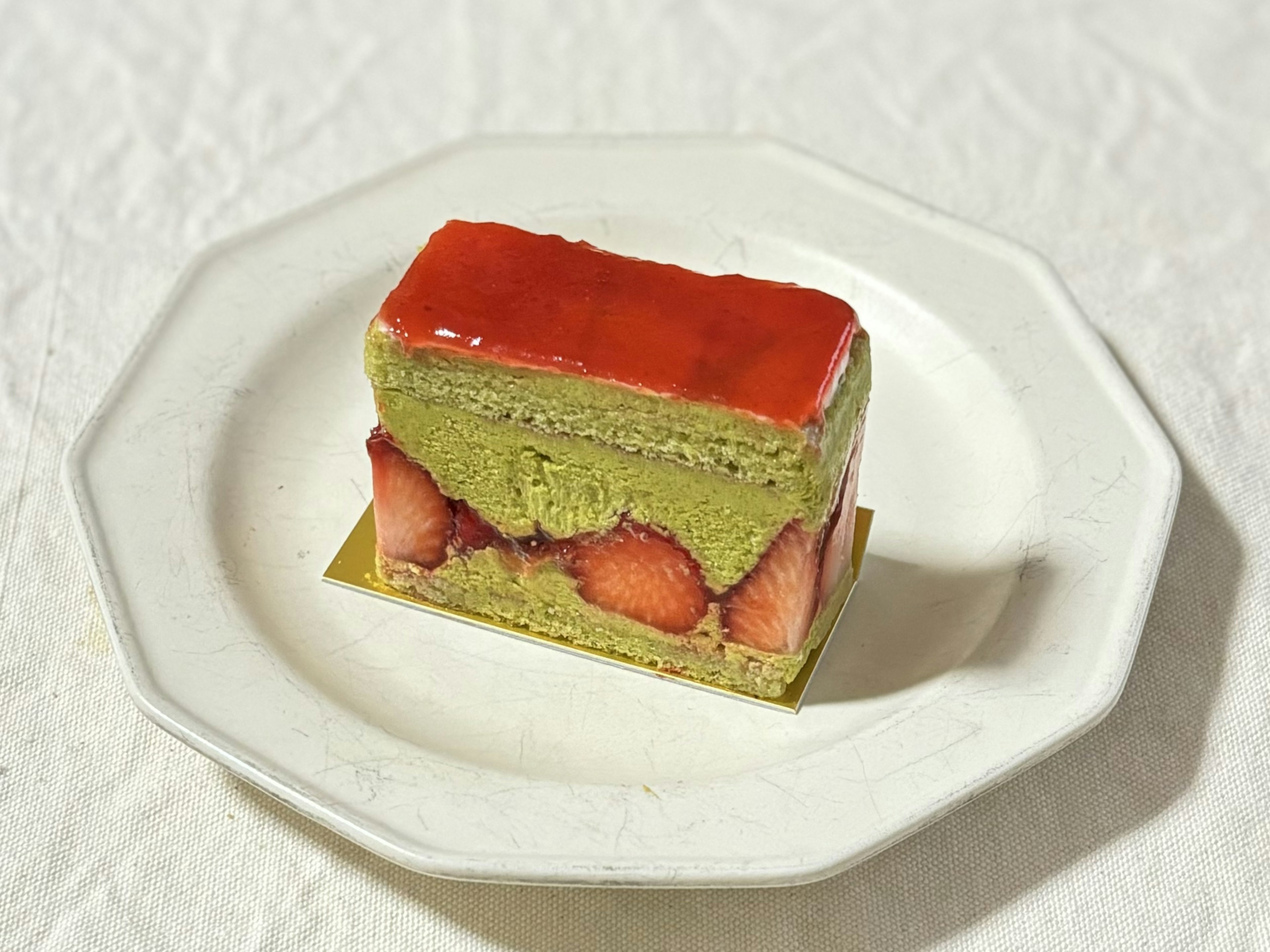 Schichttorte mit Matcha und Erdbeeren, überzogen mit einem roten Zuckerguss