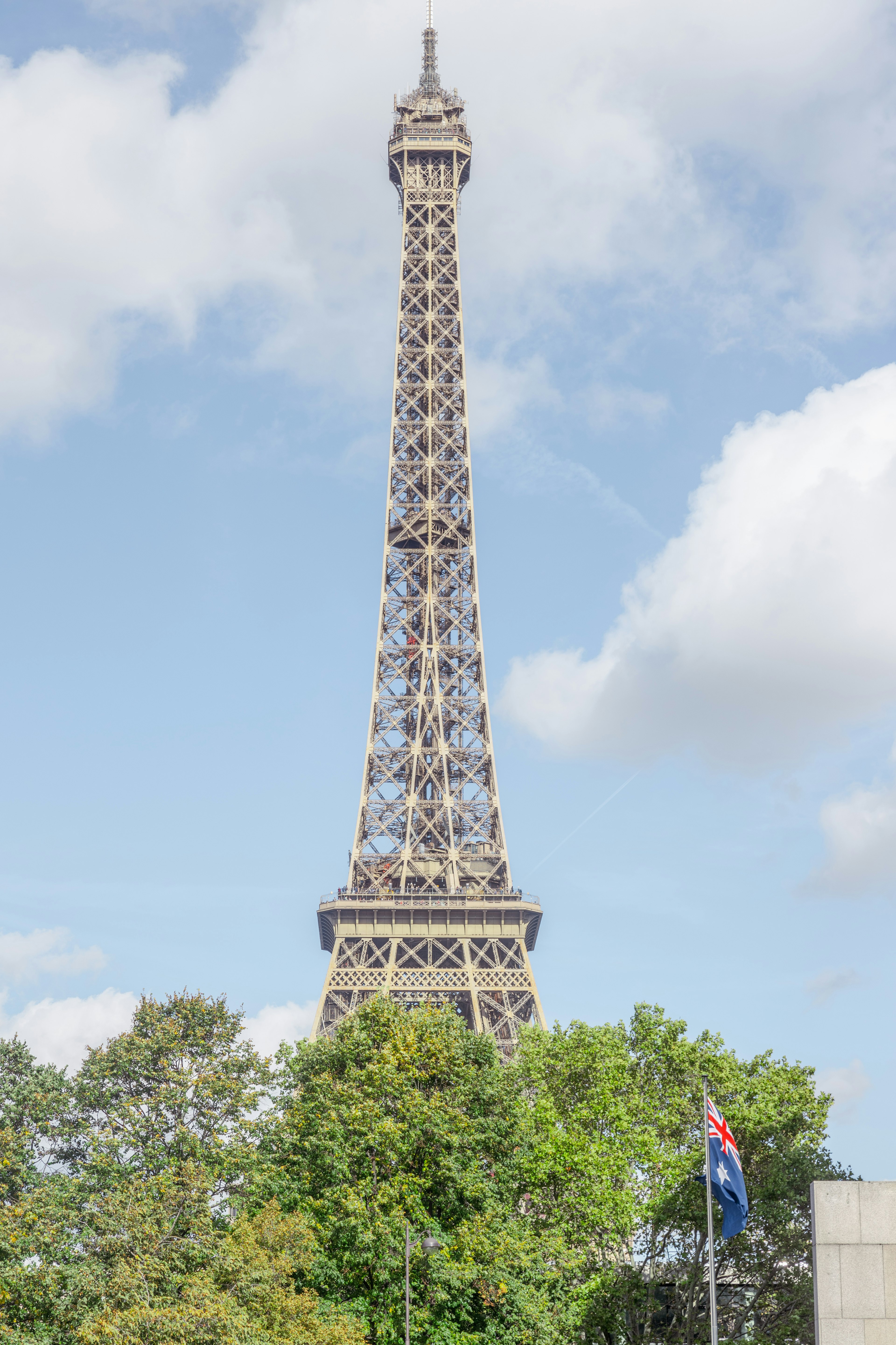 Eiffel Tower with blue sky and green trees French flag visible