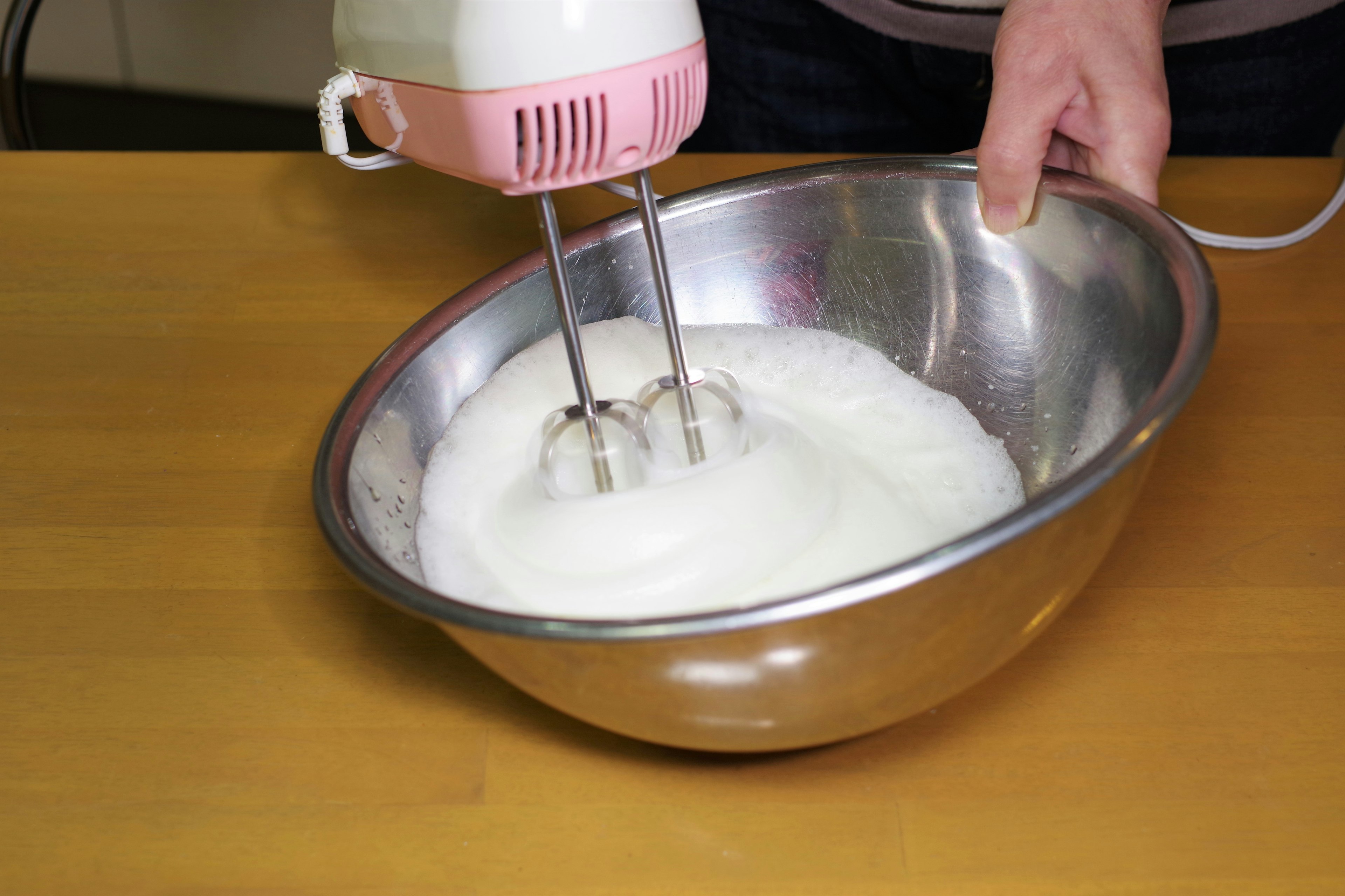 A stainless steel bowl with whipped cream being mixed by a hand mixer