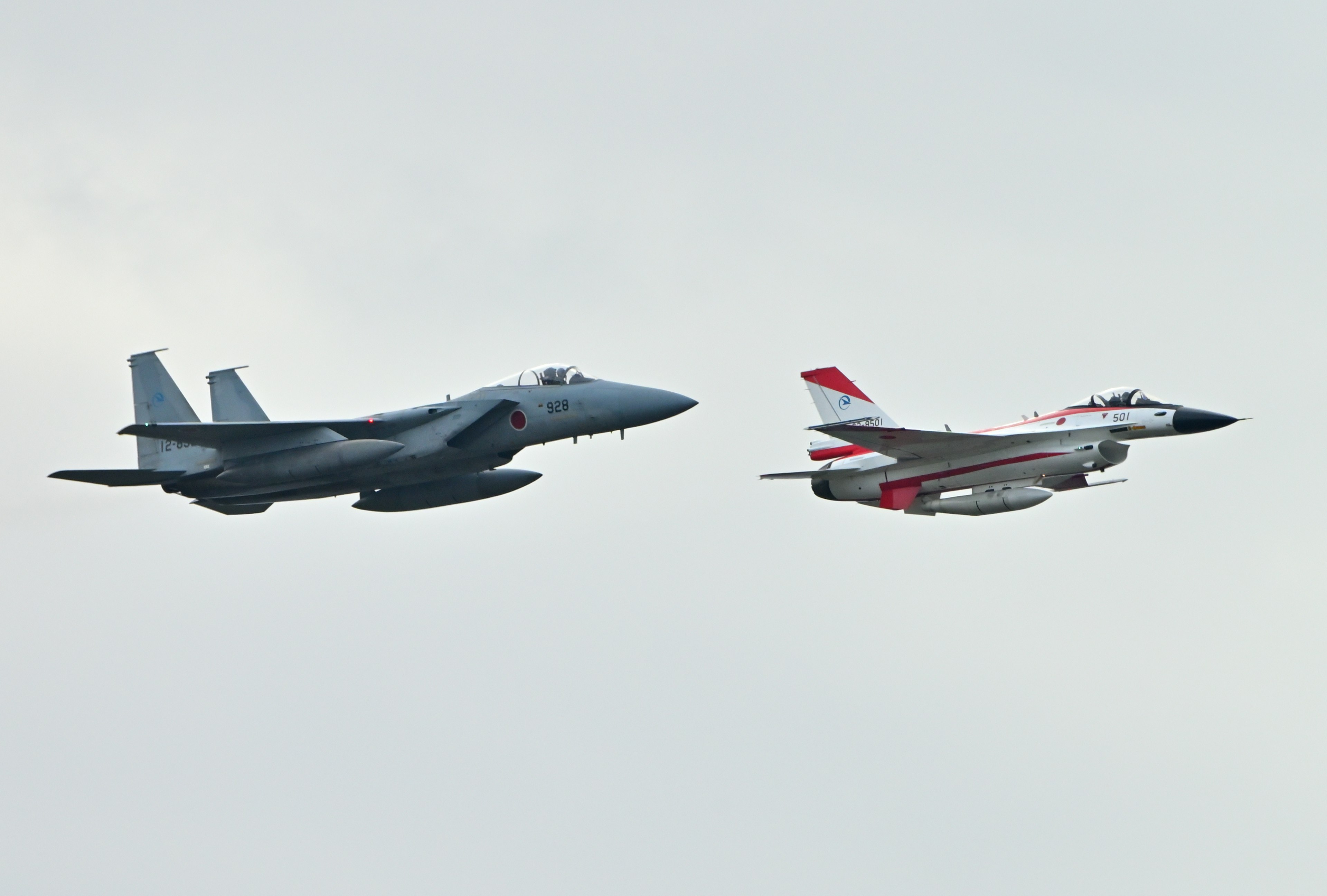 Two fighter jets flying in the sky a gray fighter jet and a red and white fighter jet flying side by side