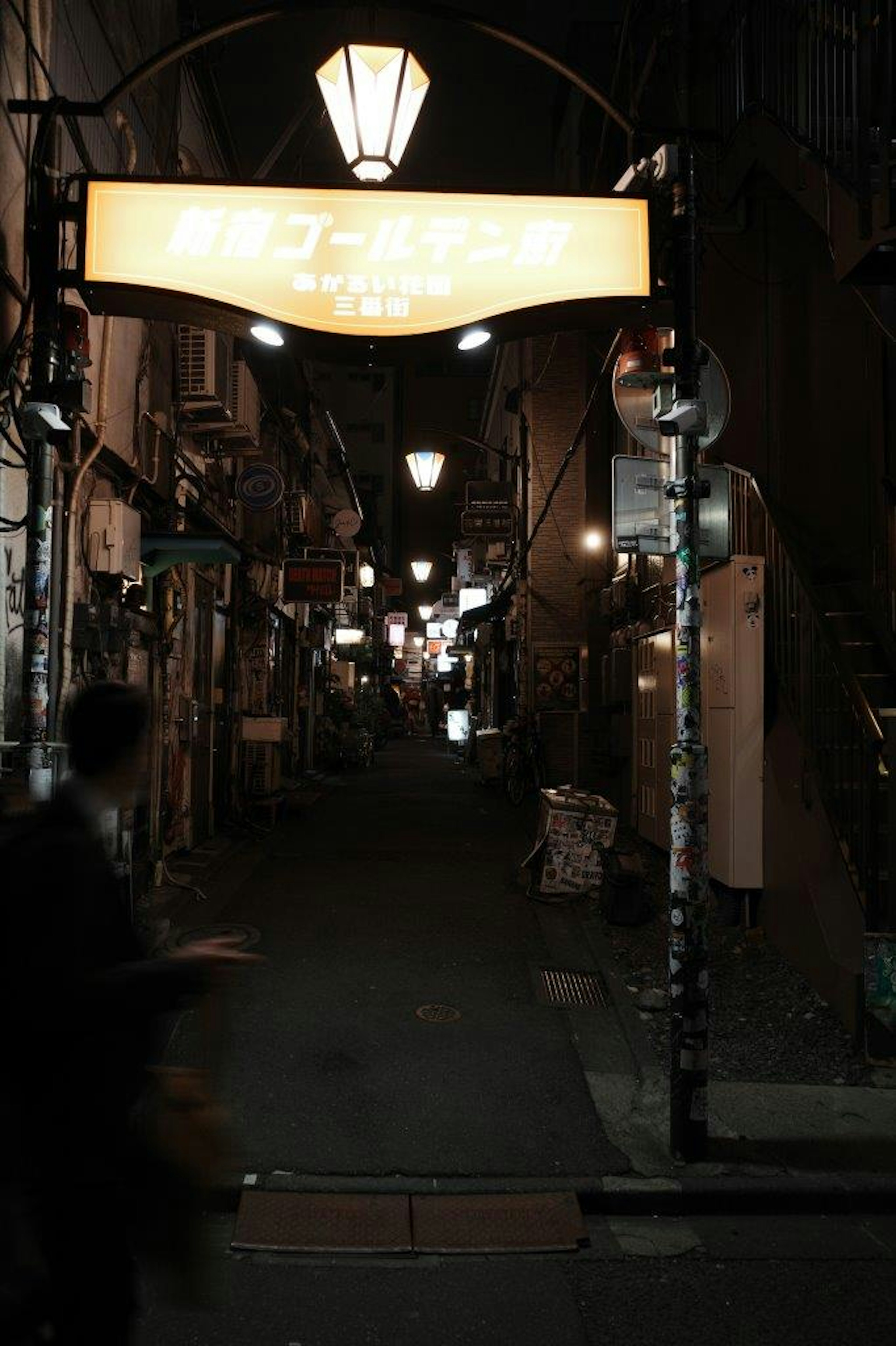 Vista nocturna de un callejón estrecho con faroles y un cartel