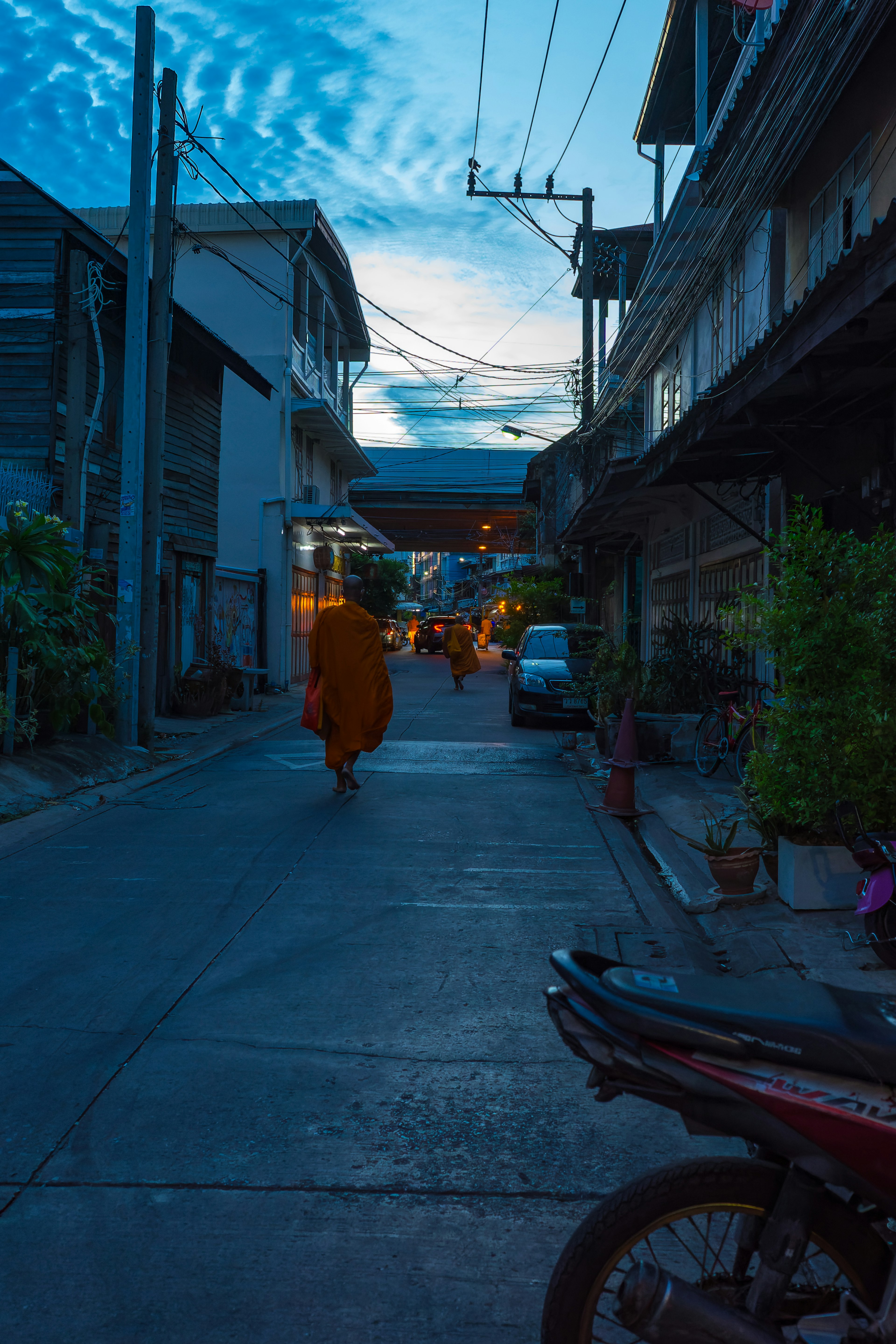 A monk walking down a quiet street at dusk with surrounding buildings