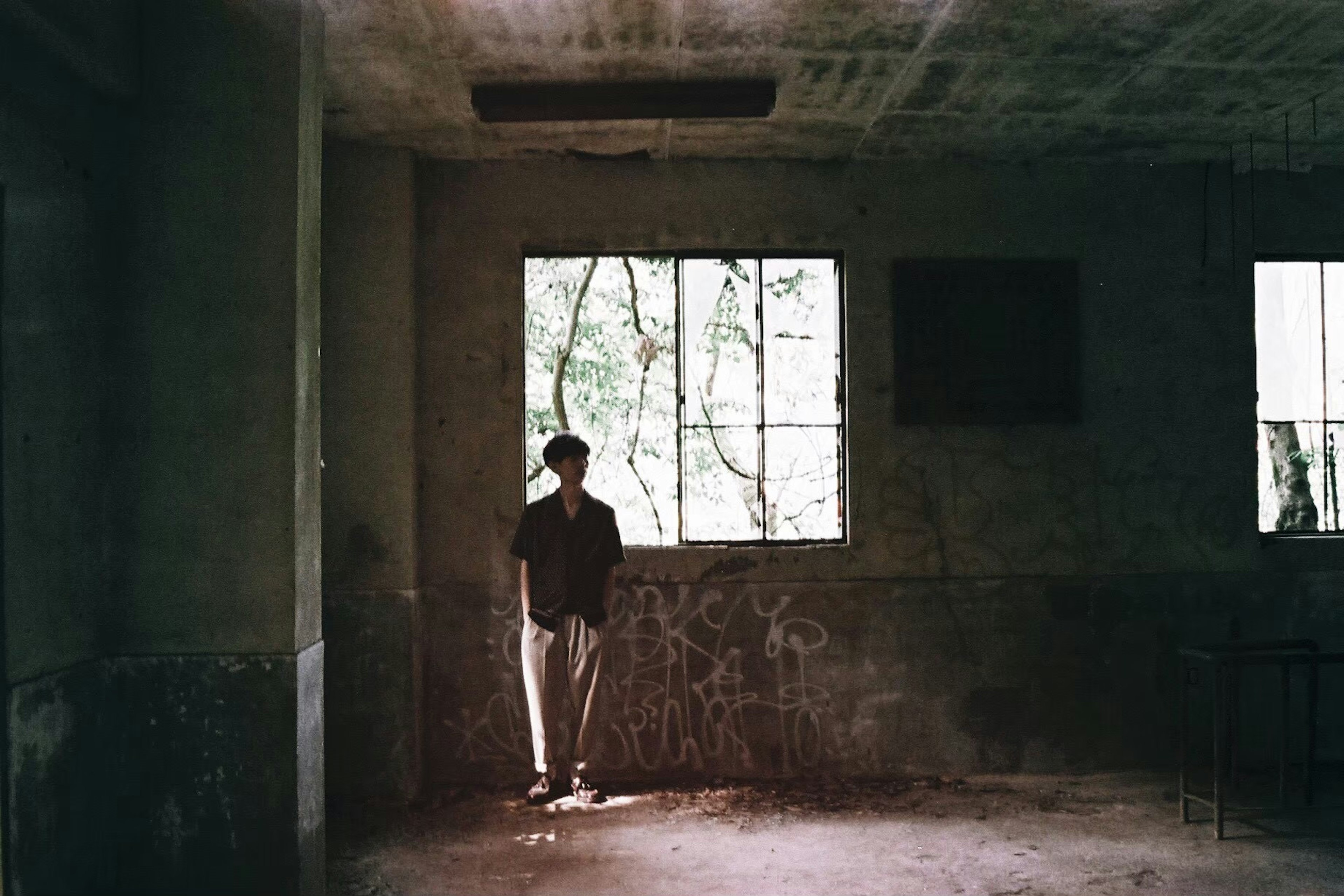 A person standing by a window in a dim room Graffiti on the walls Natural light streaming through the window