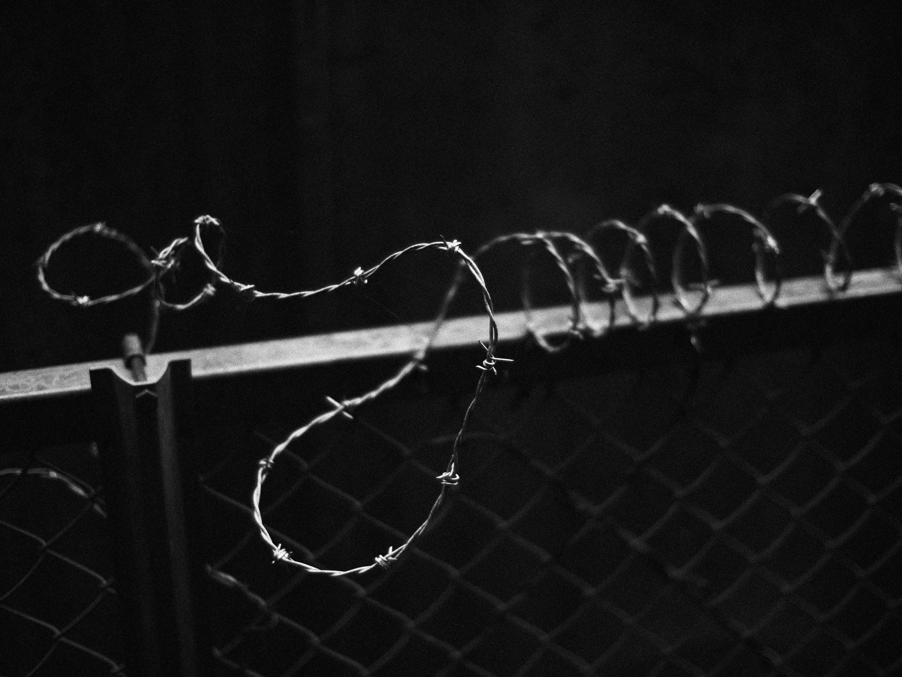 Close-up of barbed wire wrapped around a fence against a black background