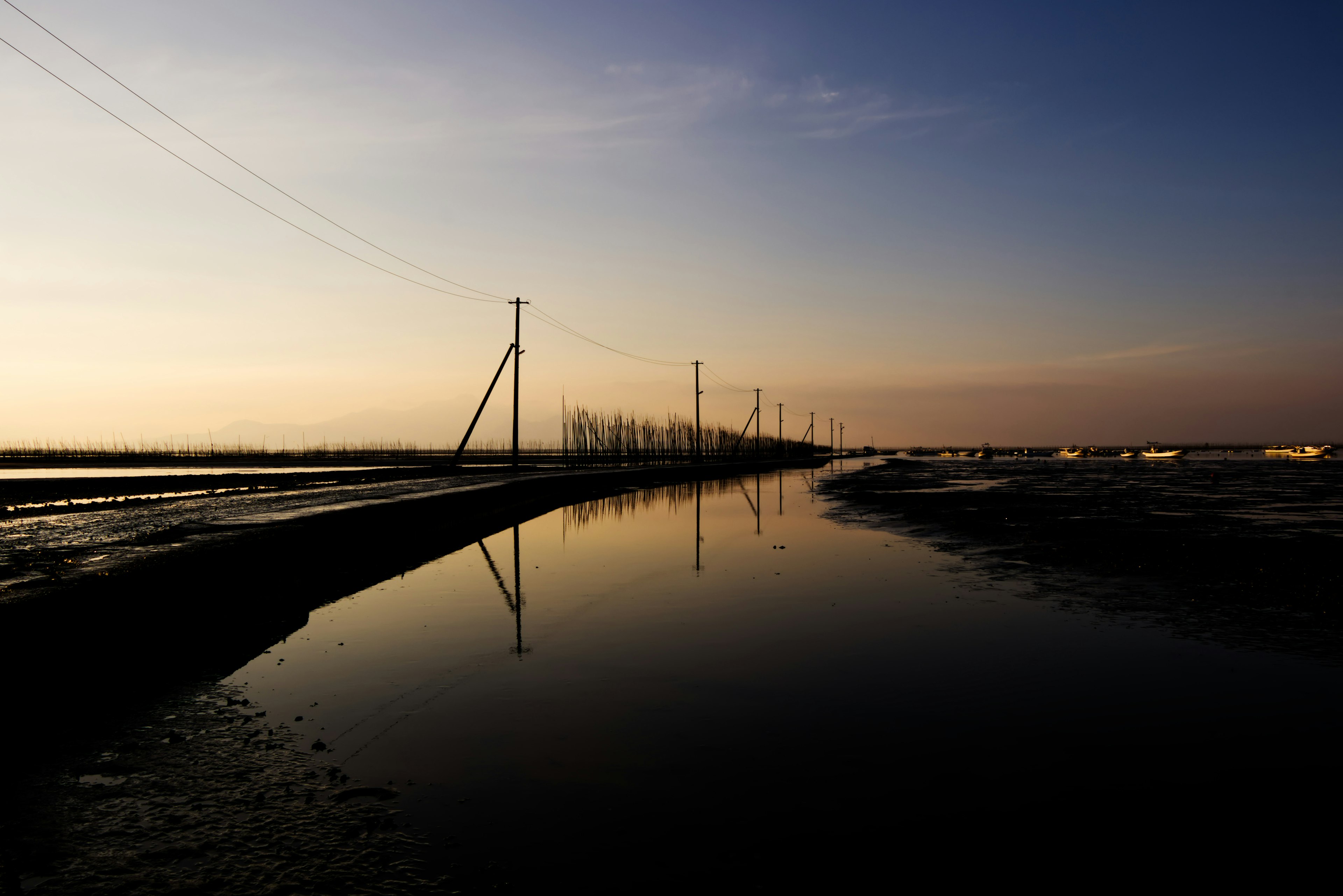 Paisaje sereno con postes de luz reflejados en agua calma al atardecer