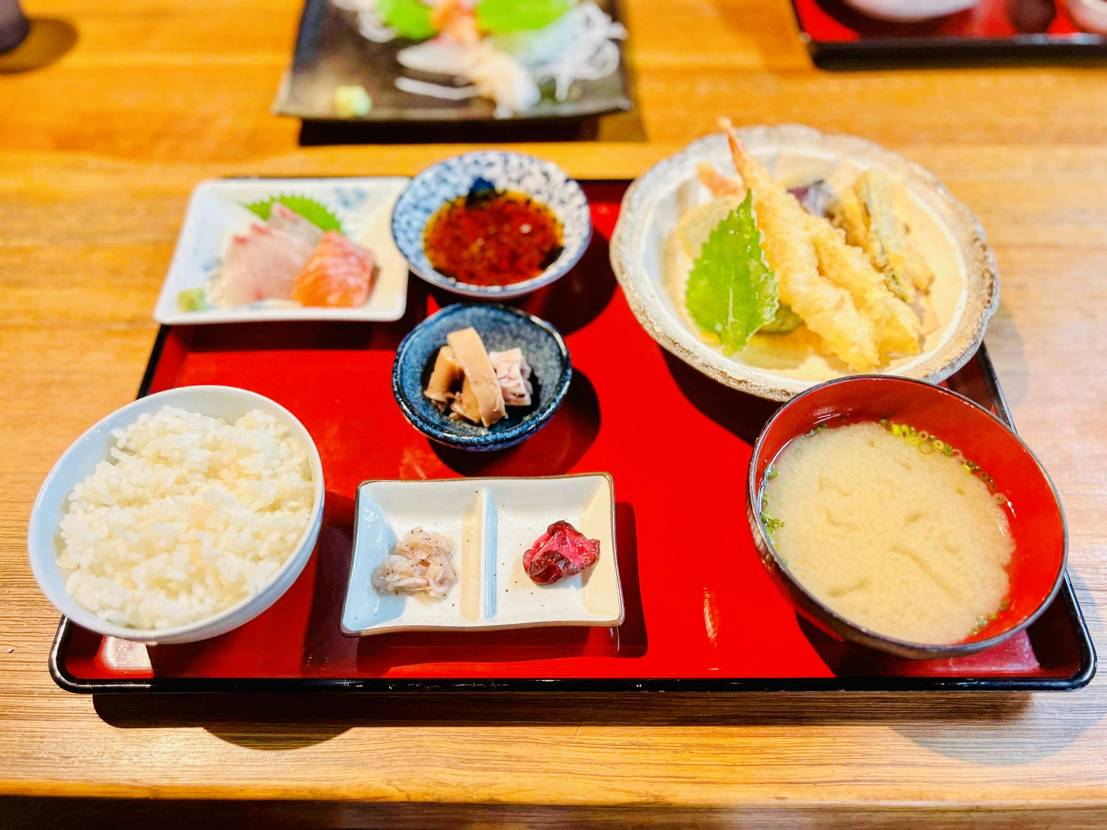 Piring tempura, sashimi, sup miso dan nasi putih di atas nampan merah