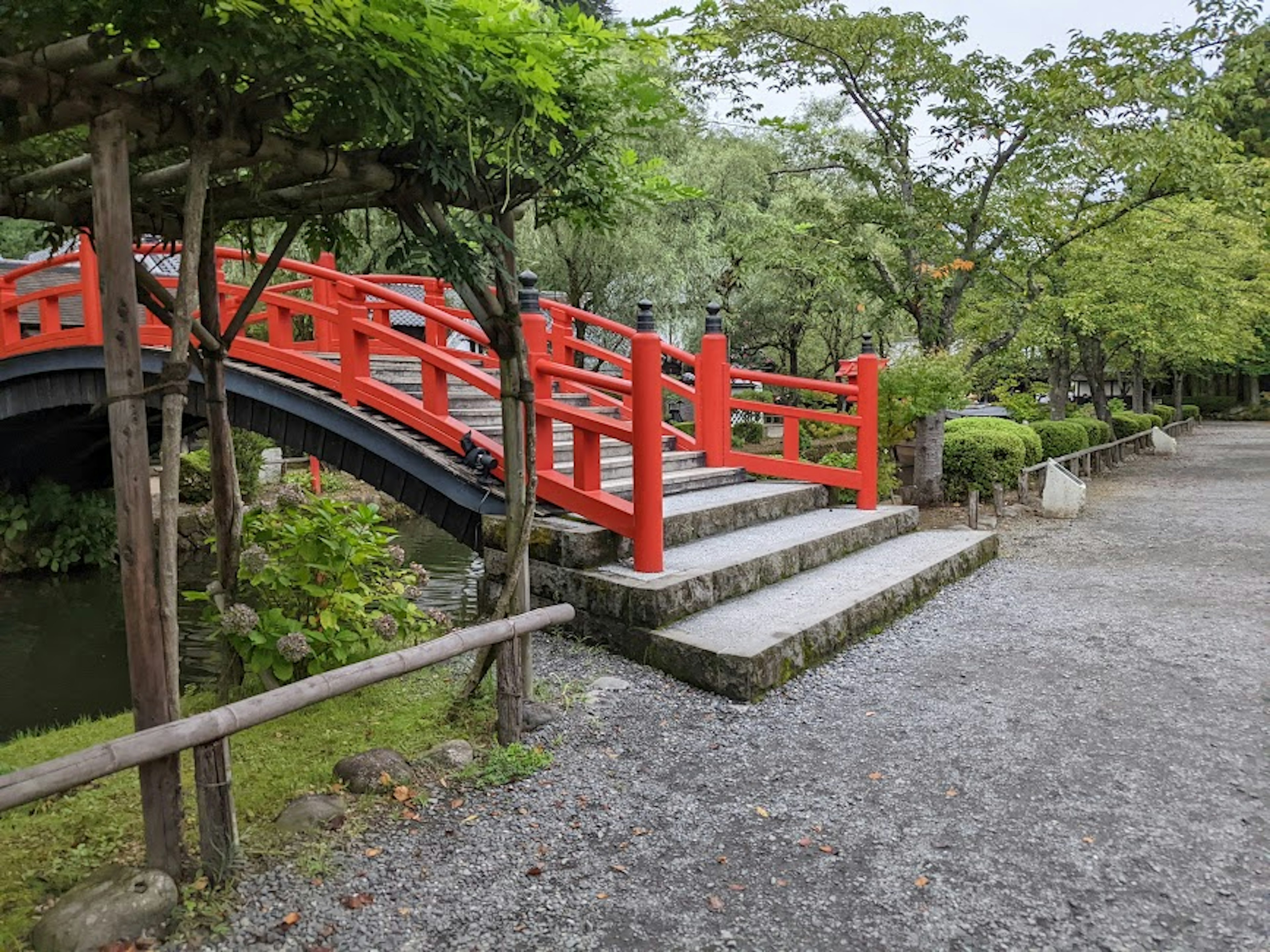 A scenic view of a red bridge and green trees in a park