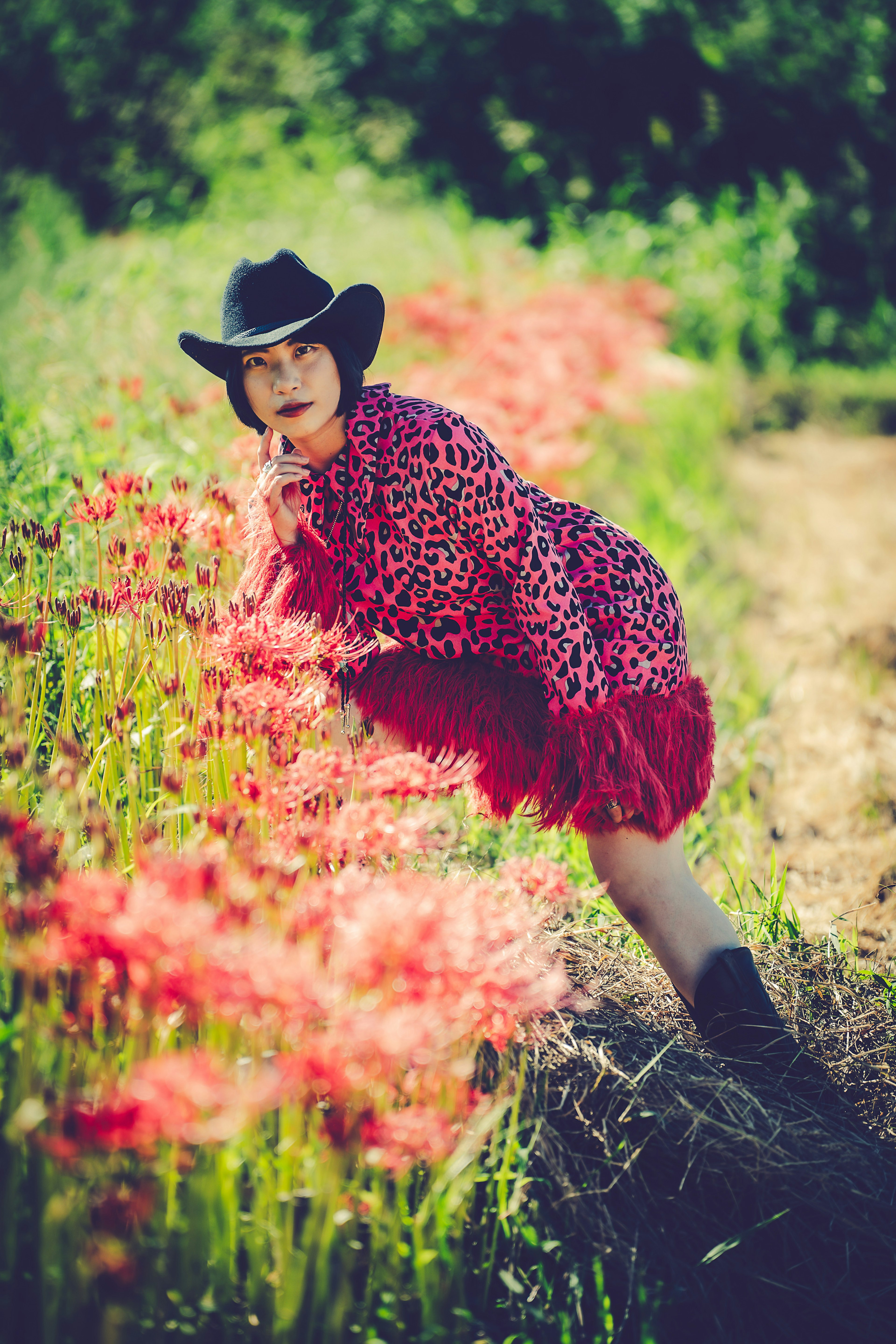 一位女性在紅色花田中擺姿勢，穿著黑色牛仔帽和紅色連衣裙