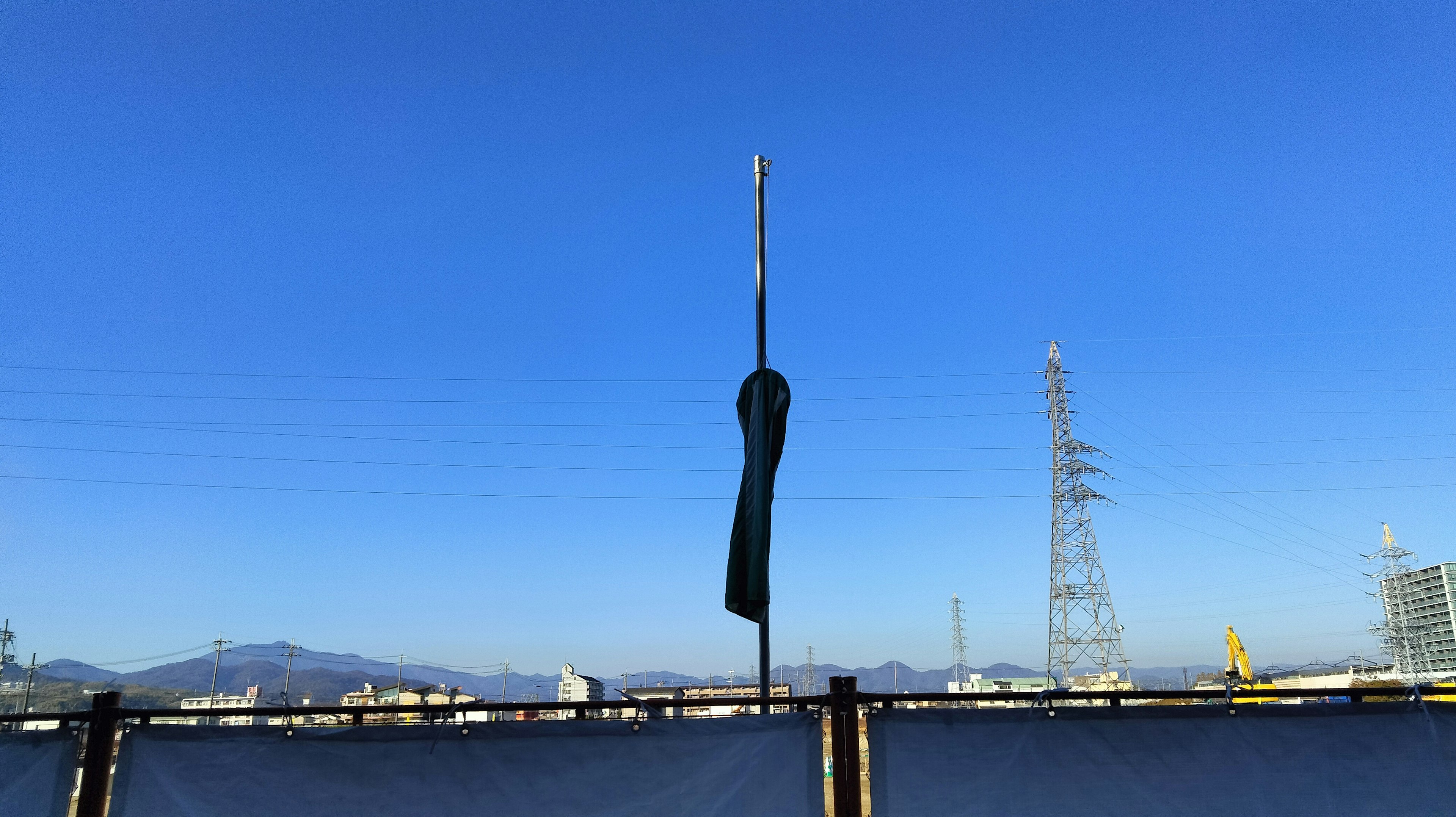 青空の下に立つ黒い旗と電柱が見える風景