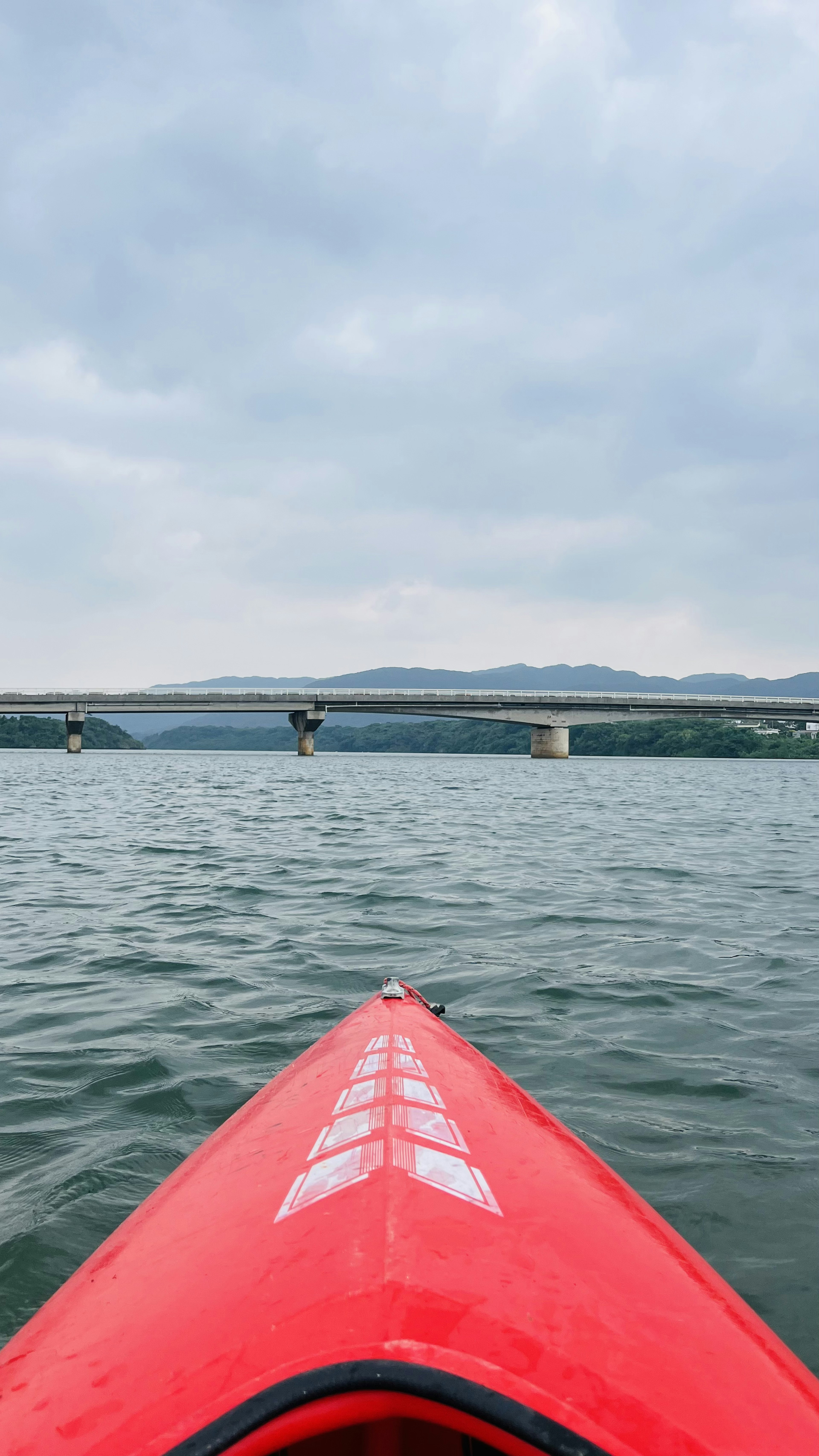 View from a red kayak on calm water with a cloudy sky