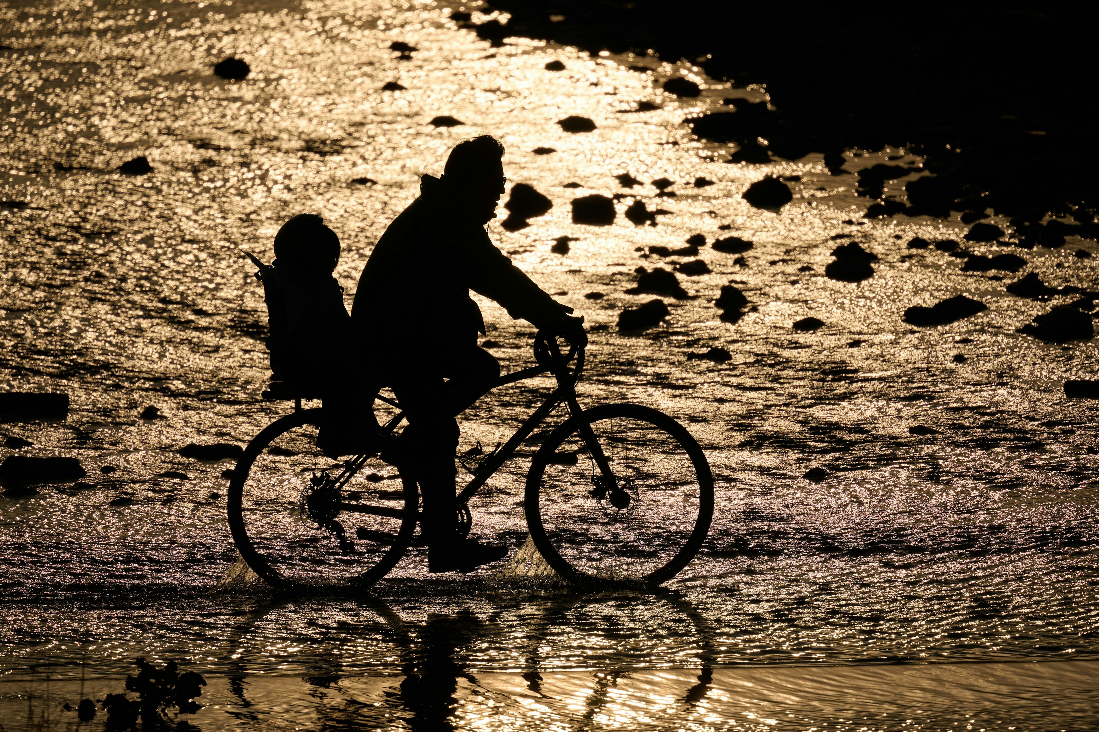 Silhouette of a person cycling with a child on the beach at sunset