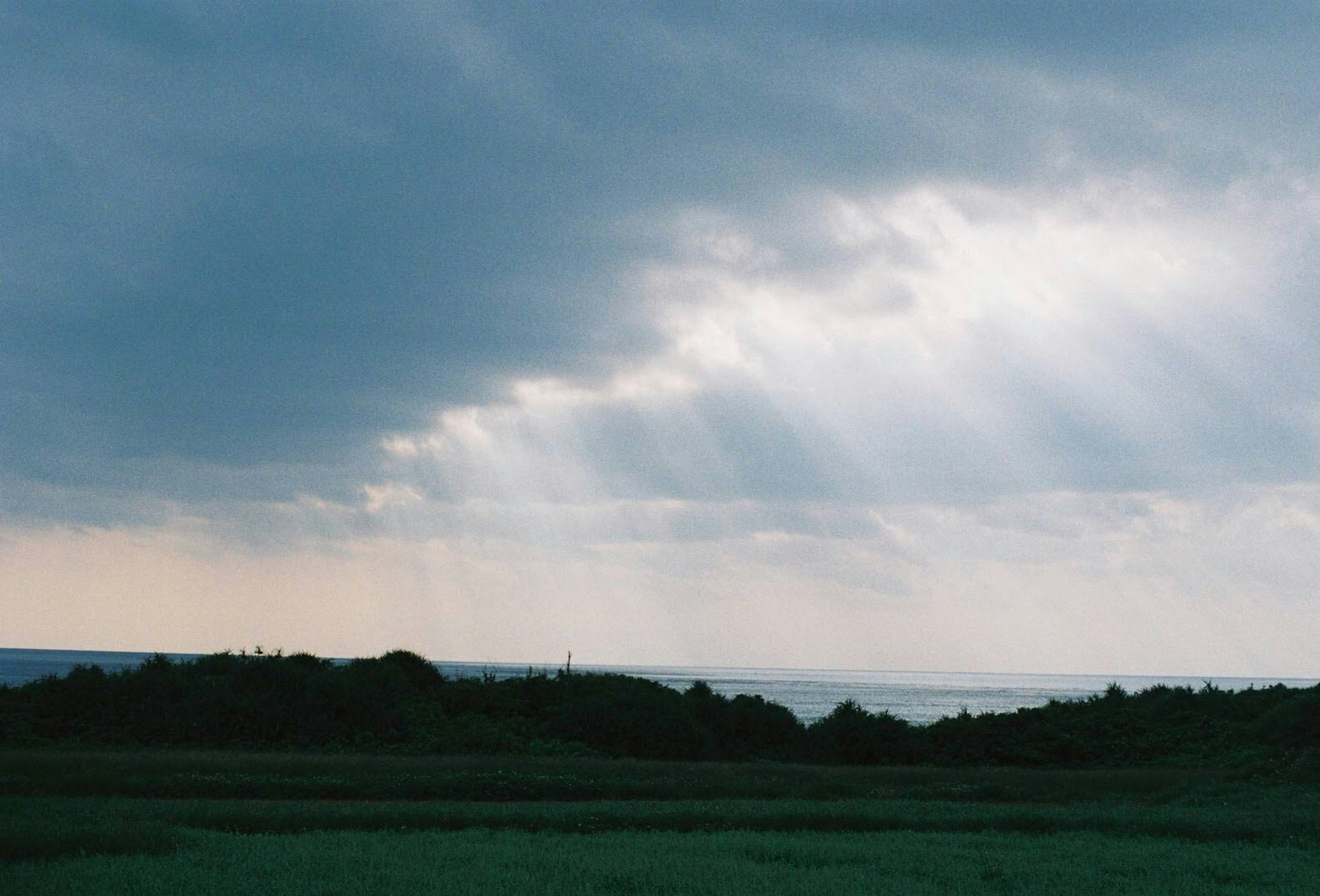 Un paysage avec des champs verts et une vue sur l'océan sous des nuages sombres avec des rayons de lumière