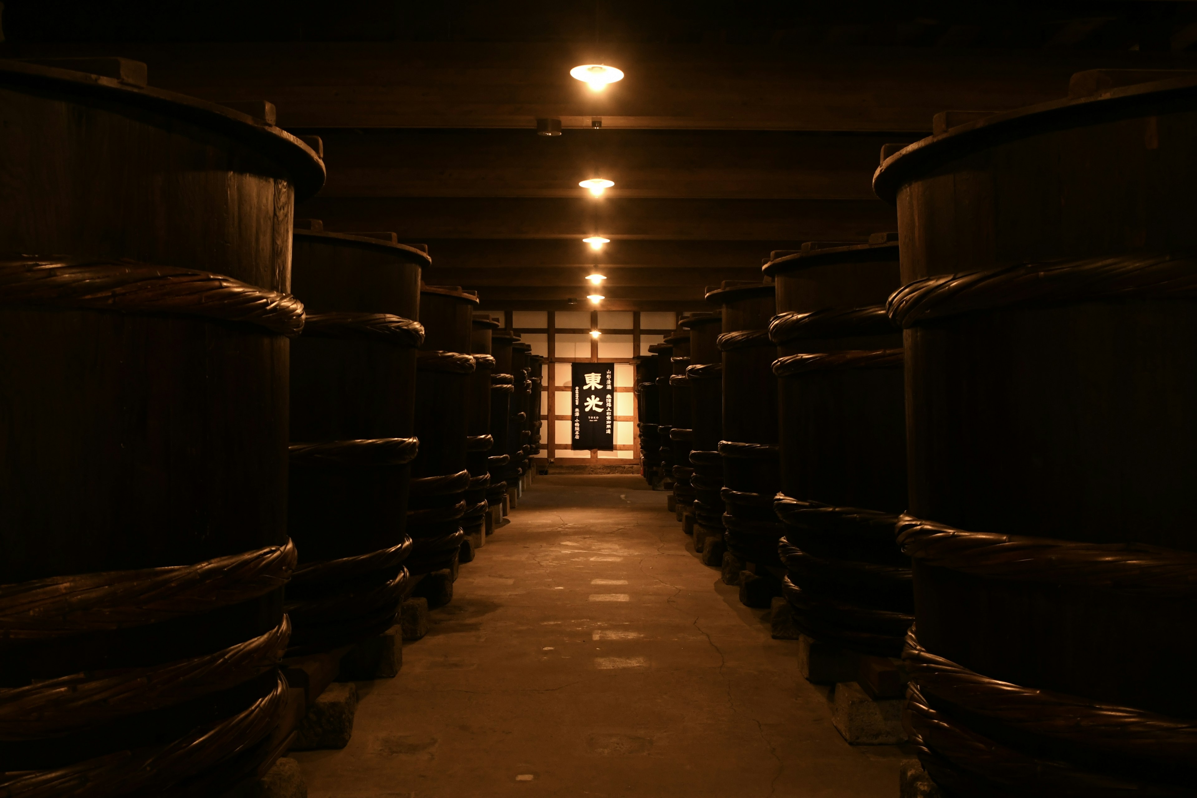 Intérieur sombre d'un entrepôt avec de grands fûts alignés et de la lumière visible au fond