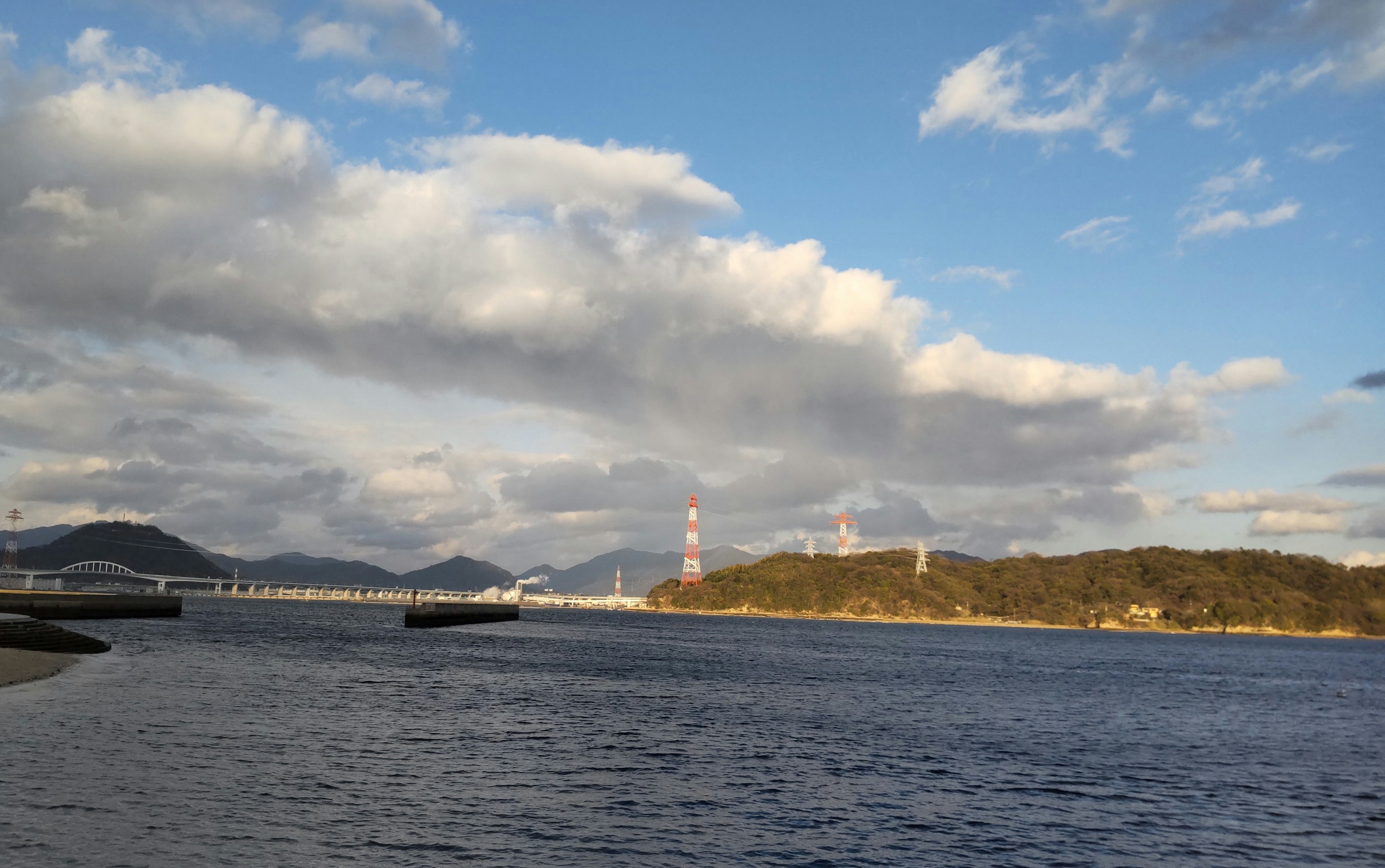 Küstenansicht mit blauem Himmel und Wolken, Brücken und Schornsteinen