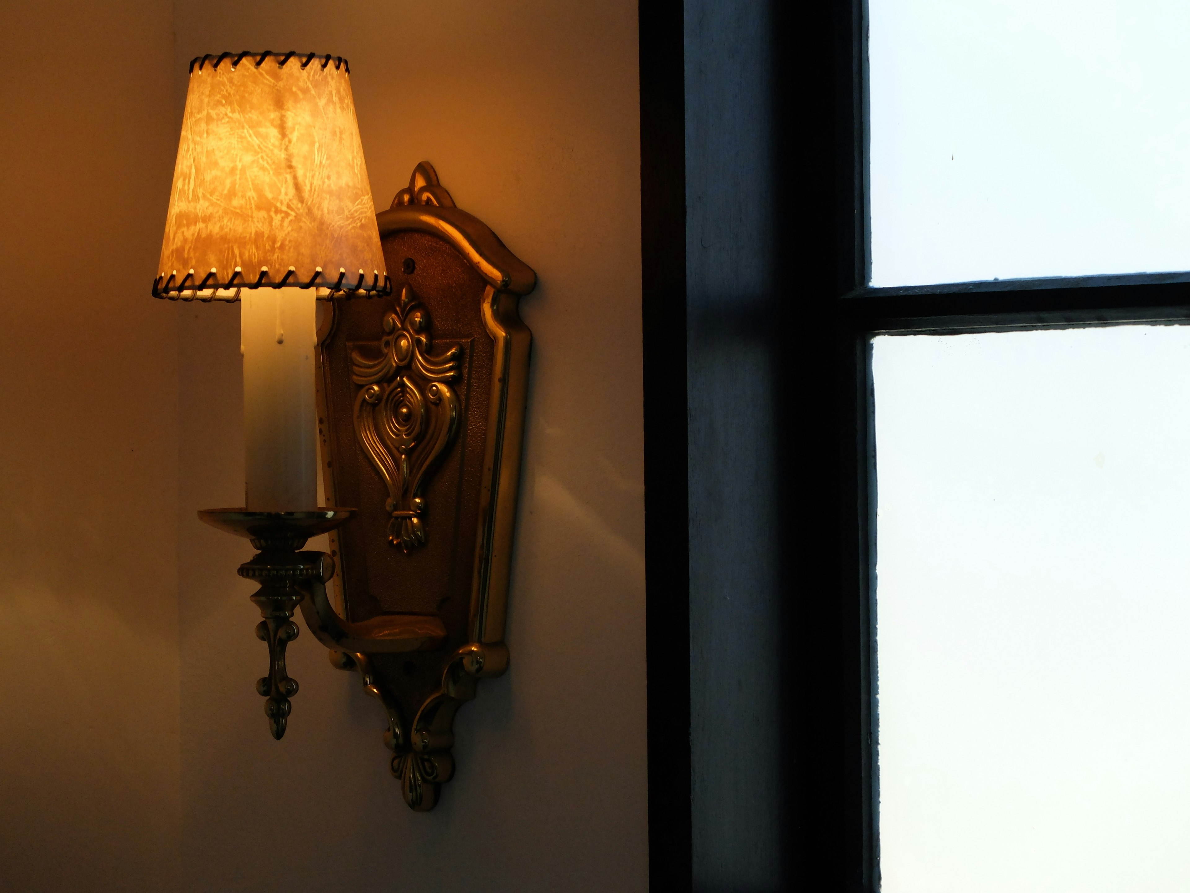 A golden wall sconce lamp with a candle and part of a window