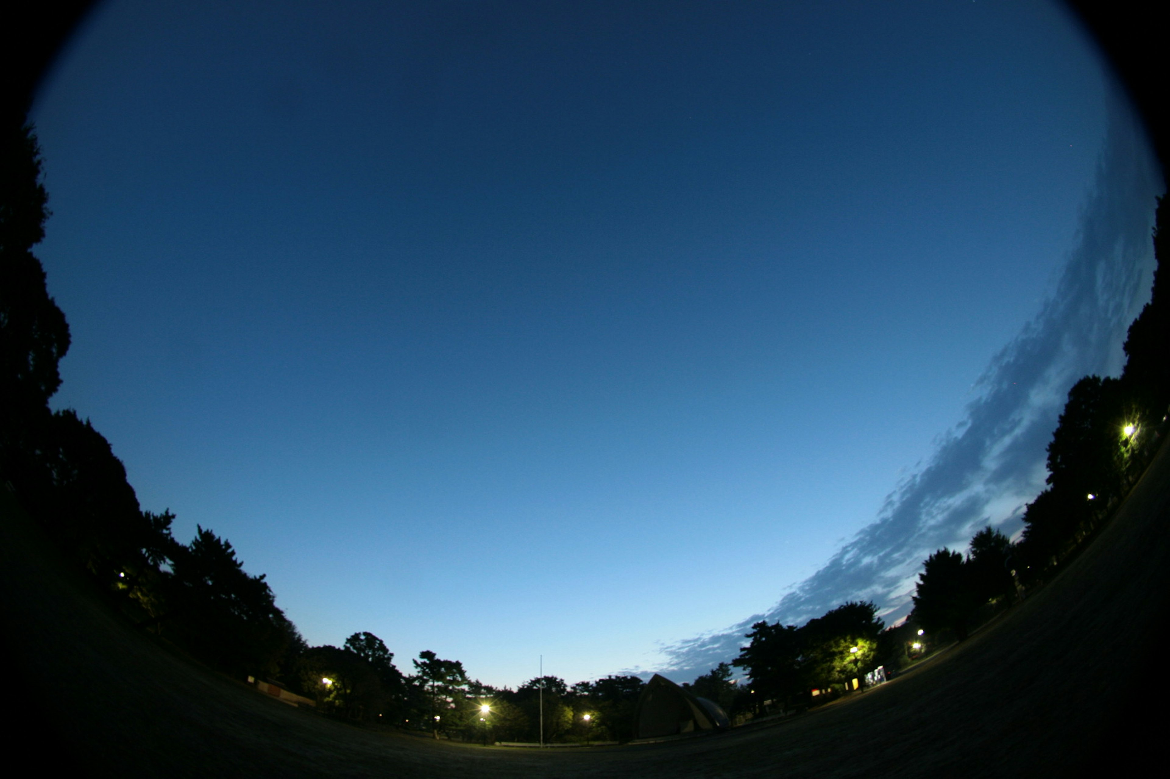 Cielo nocturno sobre un parque con luz diurna desvaneciéndose y farolas brillantes