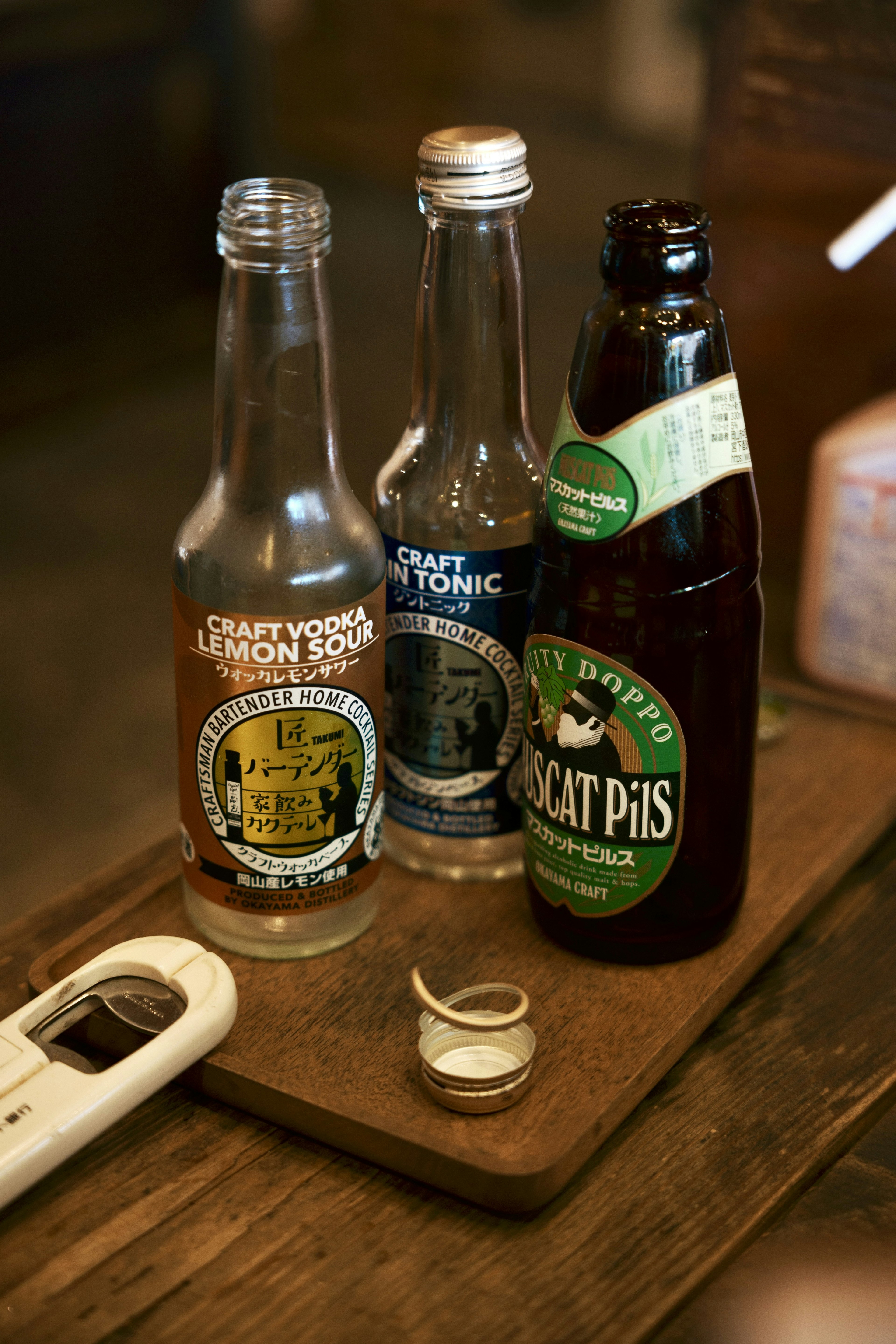 Three beverage bottles on a wooden tray with a coaster