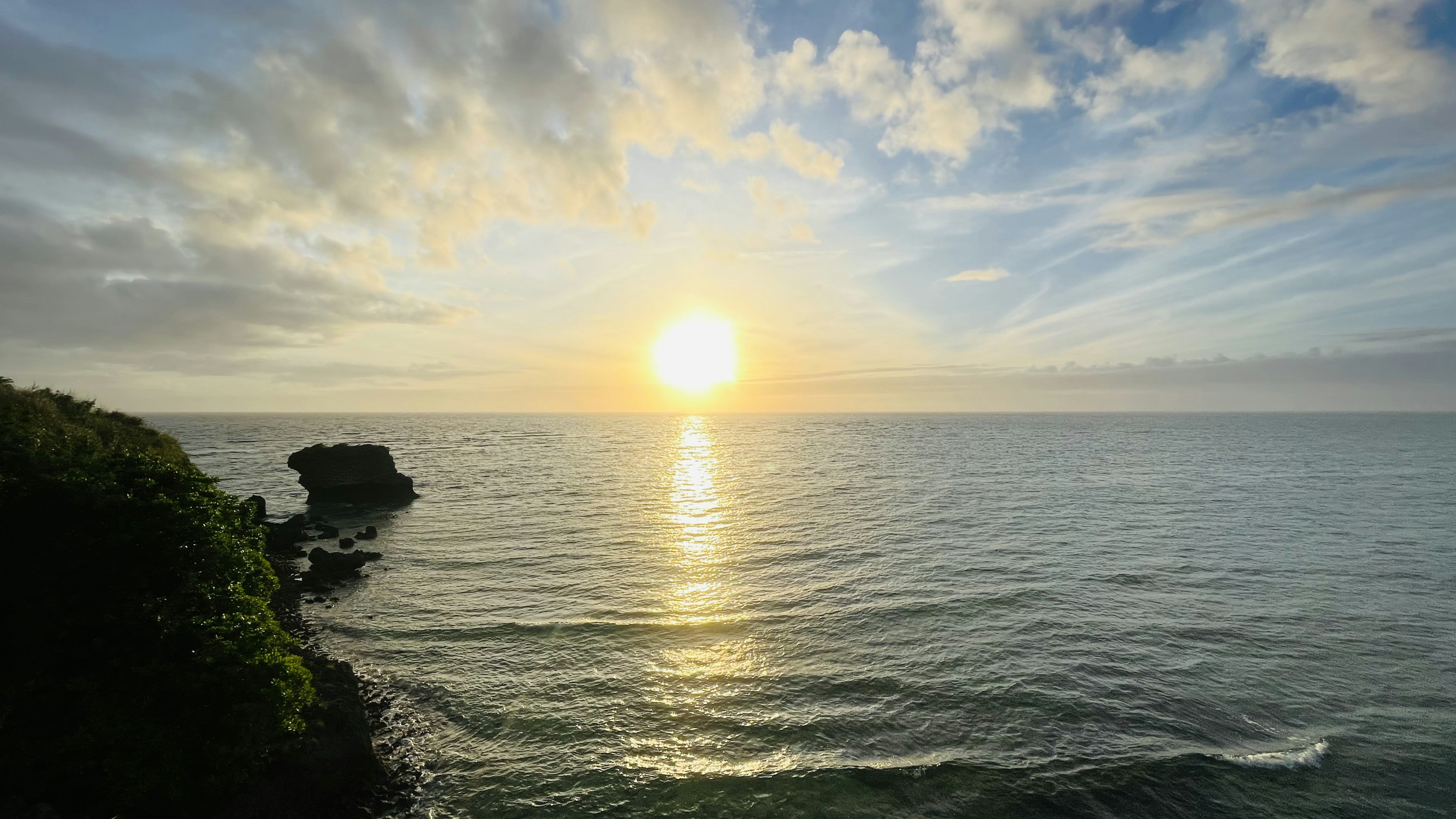 Tramonto sul mare con onde calme e costa rocciosa