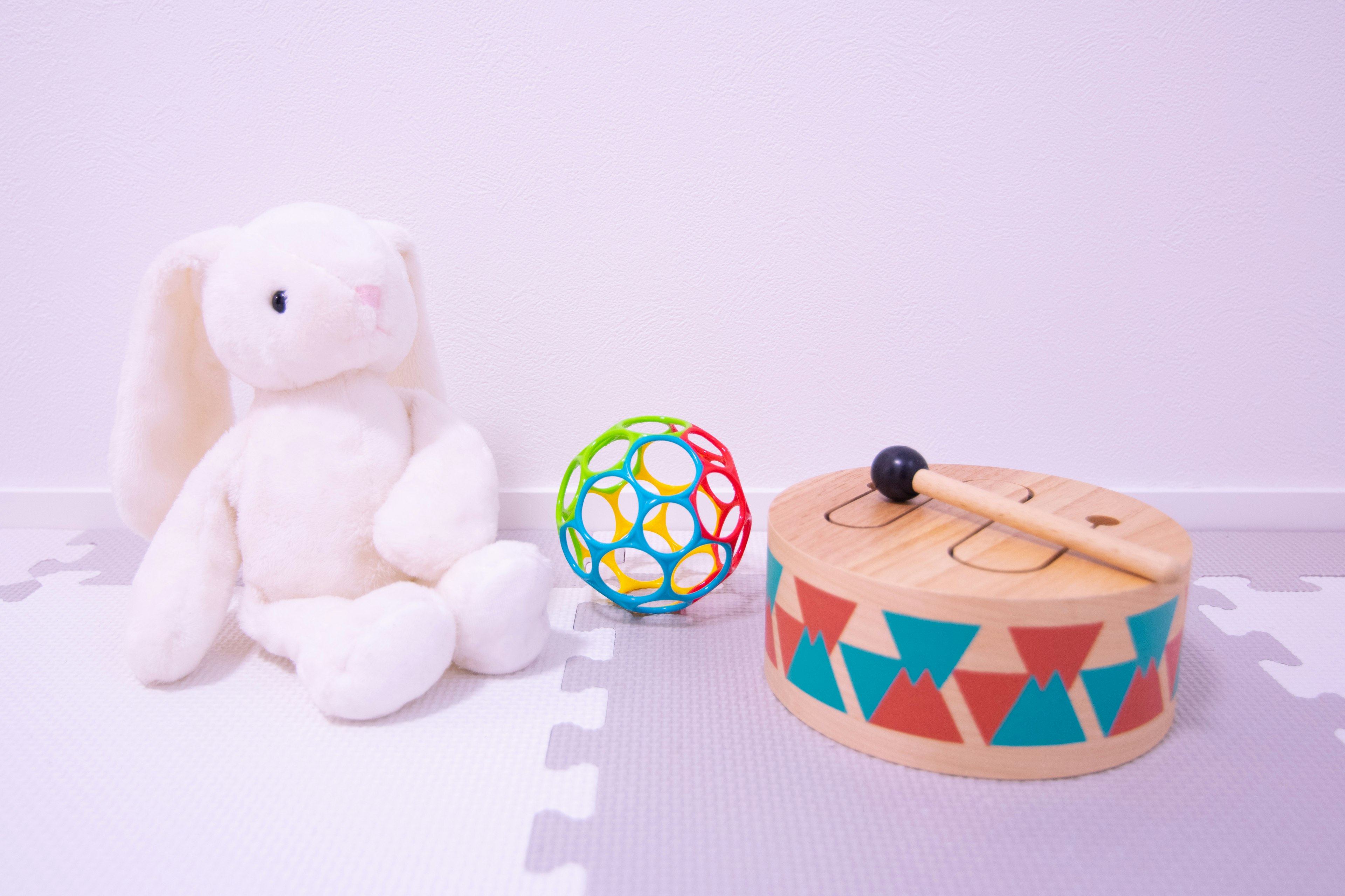 Un conejo de peluche blanco junto a una pelota colorida y un tambor de madera en una habitación infantil