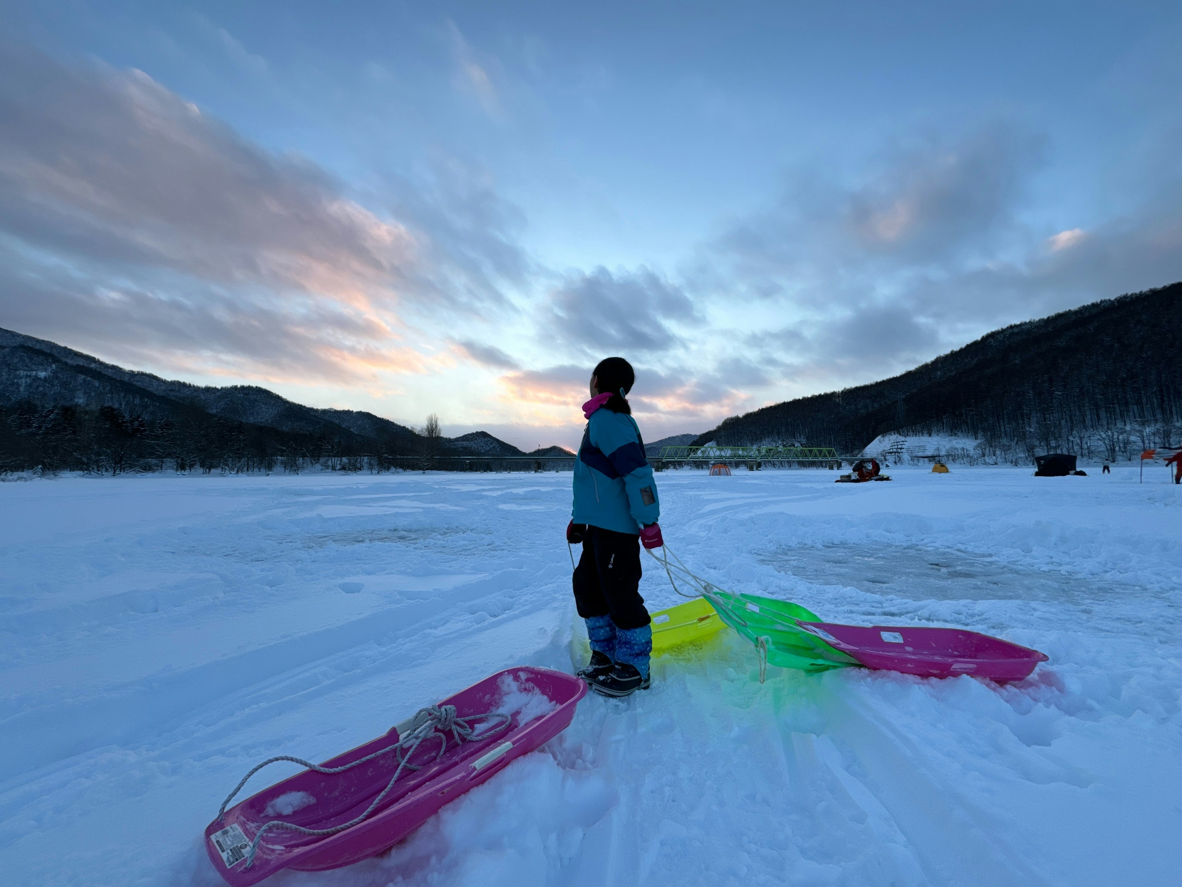 Niño de pie en la nieve con trineos coloridos en un paisaje invernal