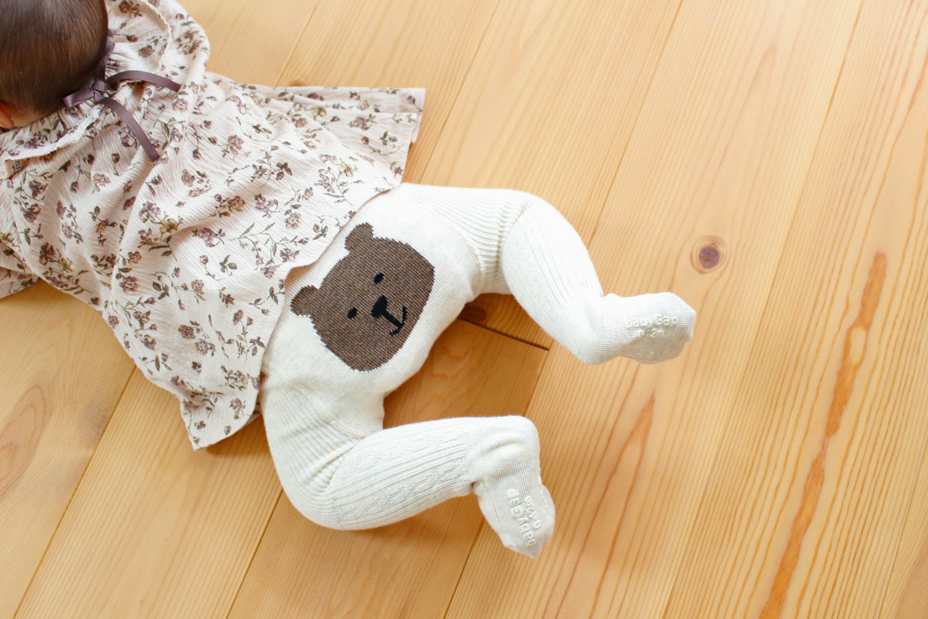 Baby lying on wooden floor wearing white pants with bear design on the back