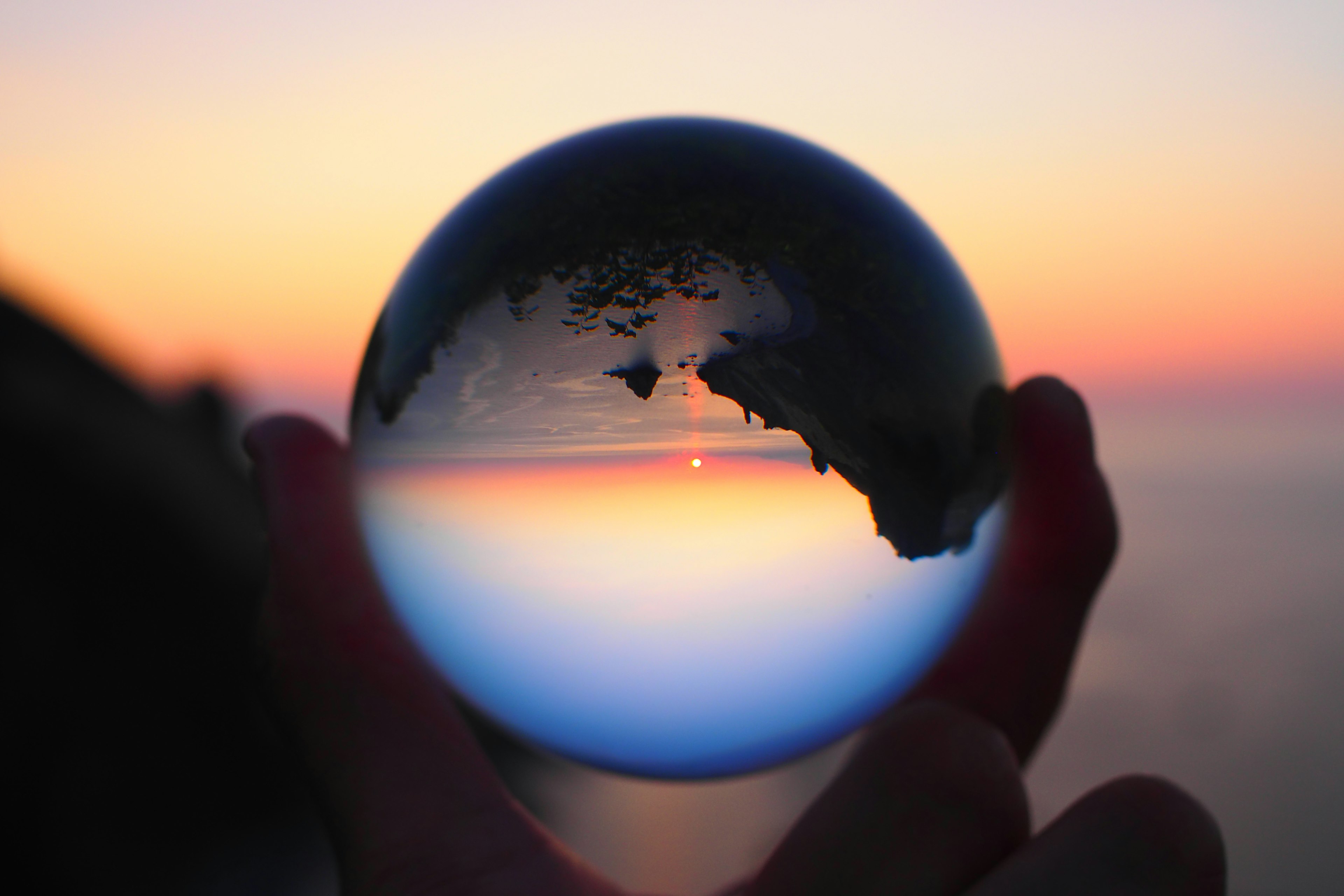 Une main tenant une boule en cristal reflétant un coucher de soleil