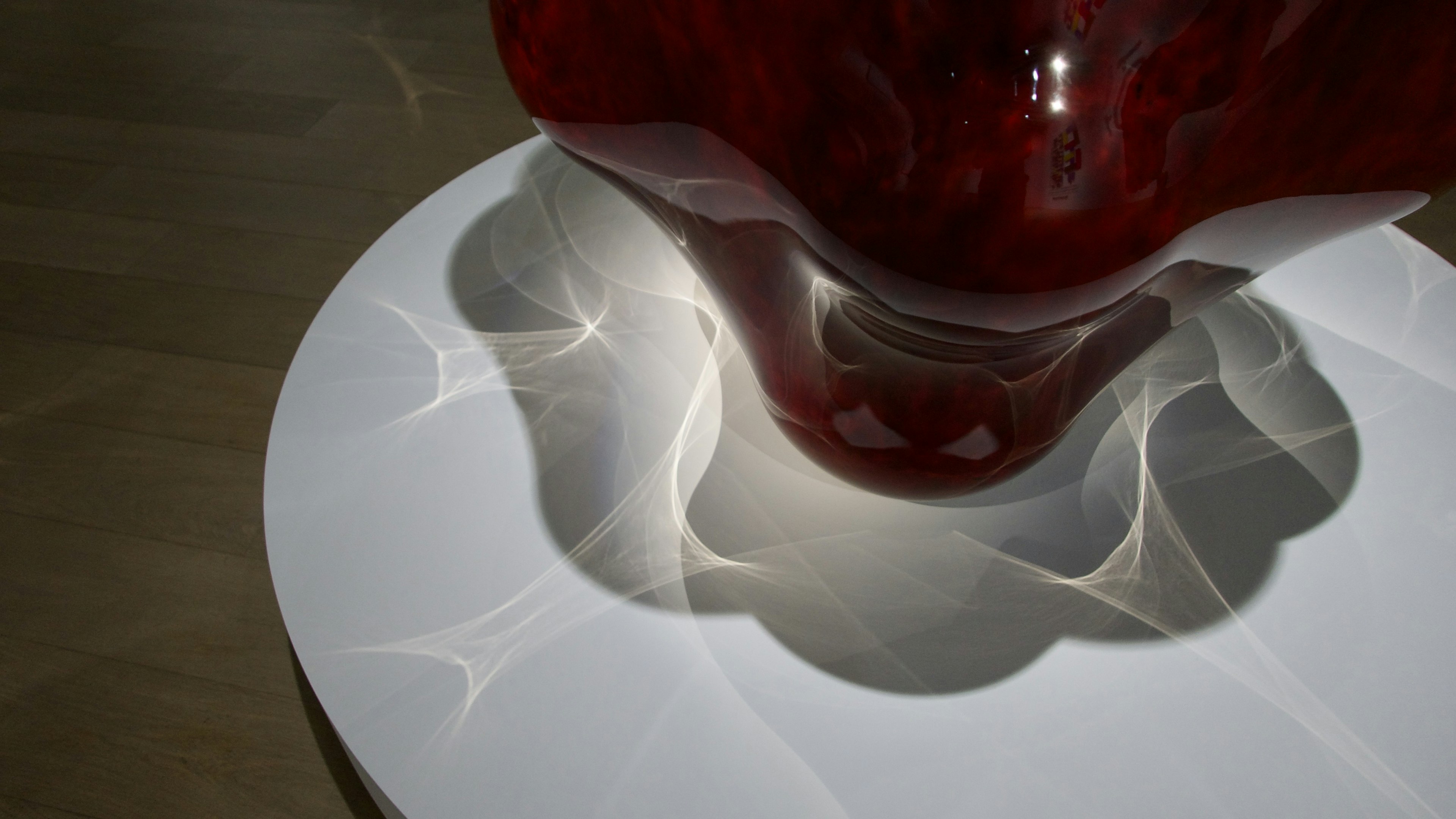 Red sculpture casting intricate shadows on a white pedestal