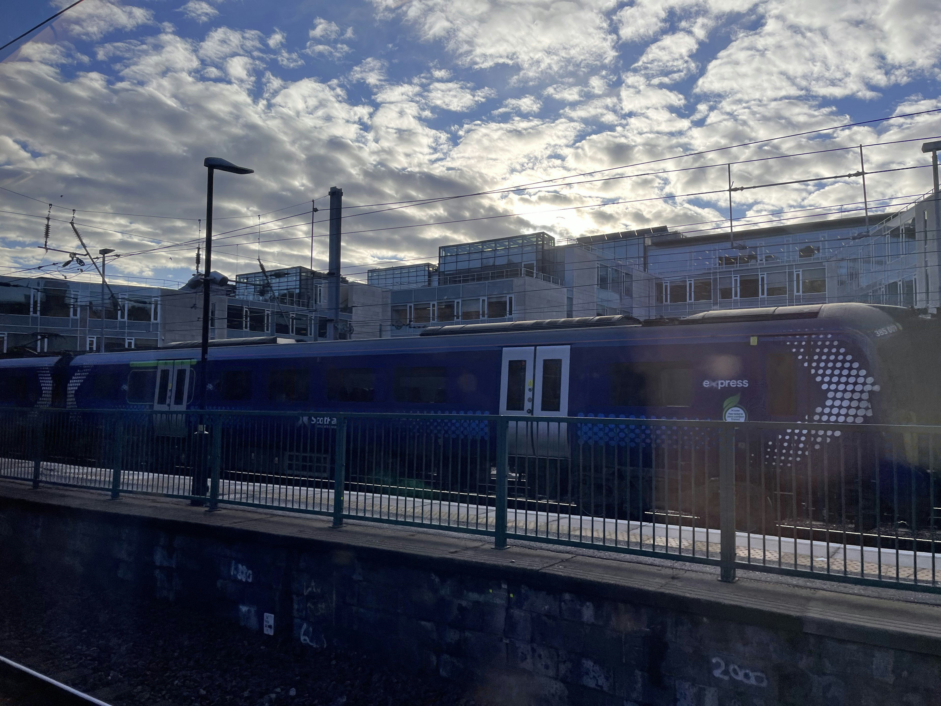 Blue train parked at a station with a cloudy sky in the background