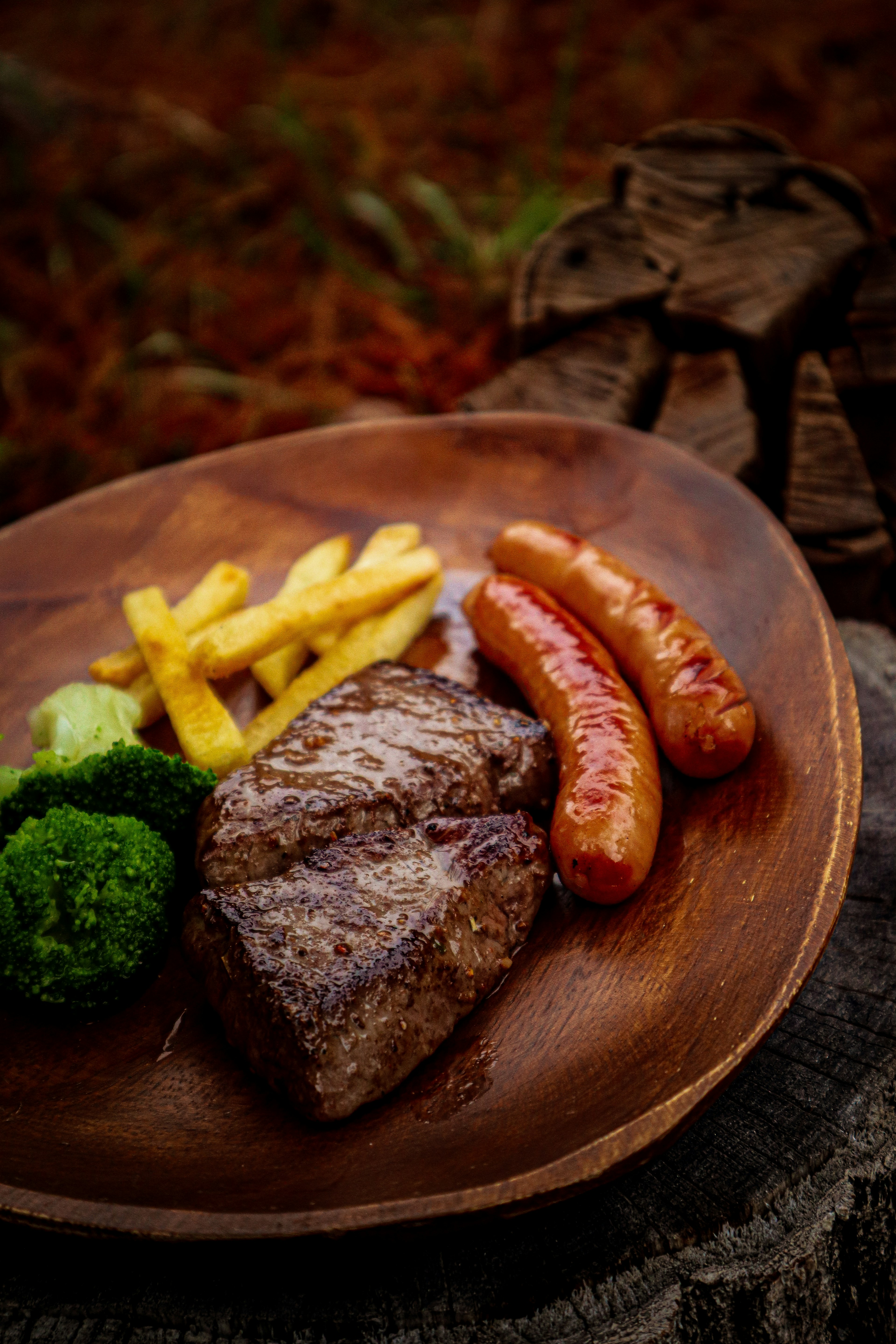 Steak and sausages served on a wooden plate with fries and broccoli