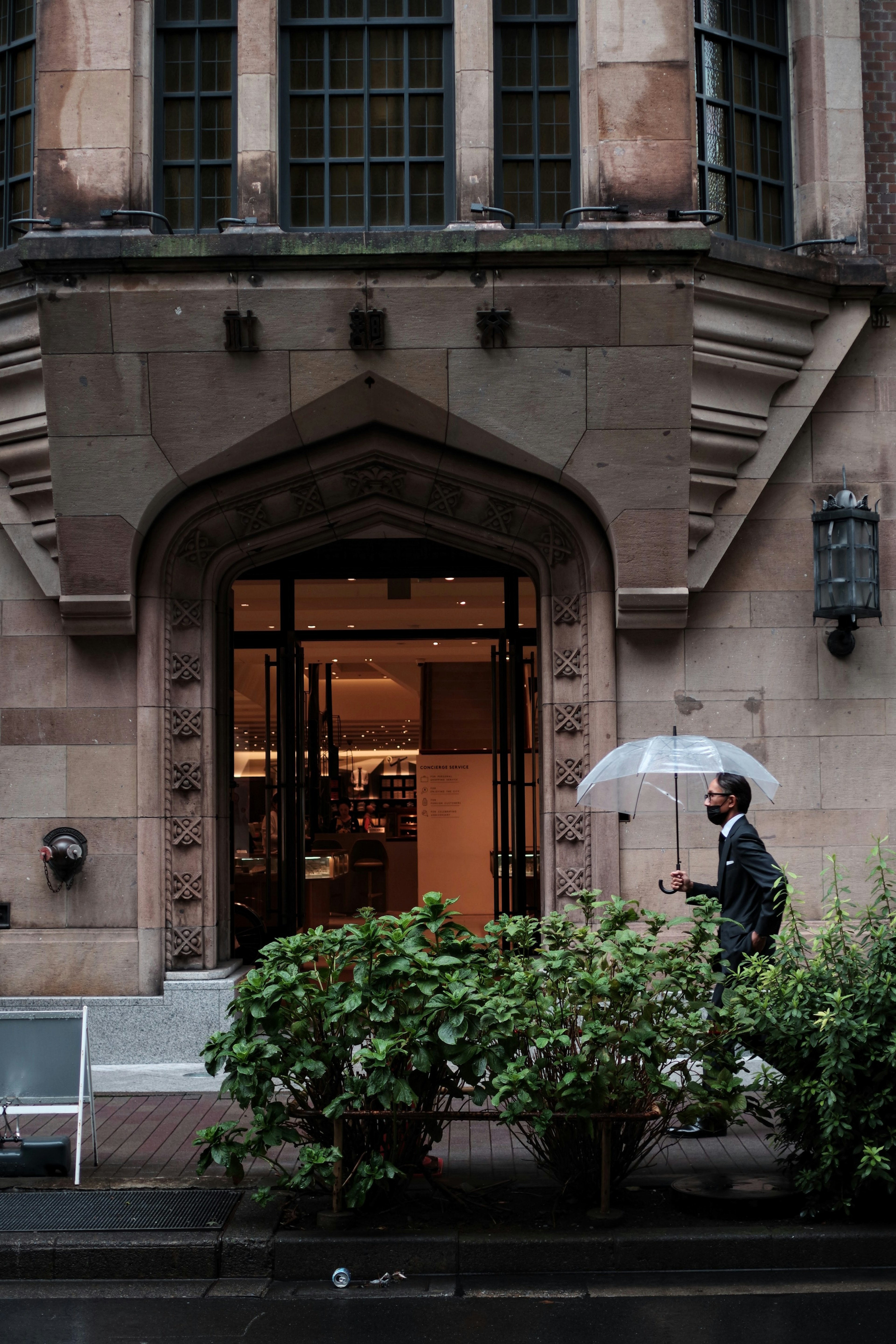 一個拿著傘的男人在雨中走過一棟古老的建築前