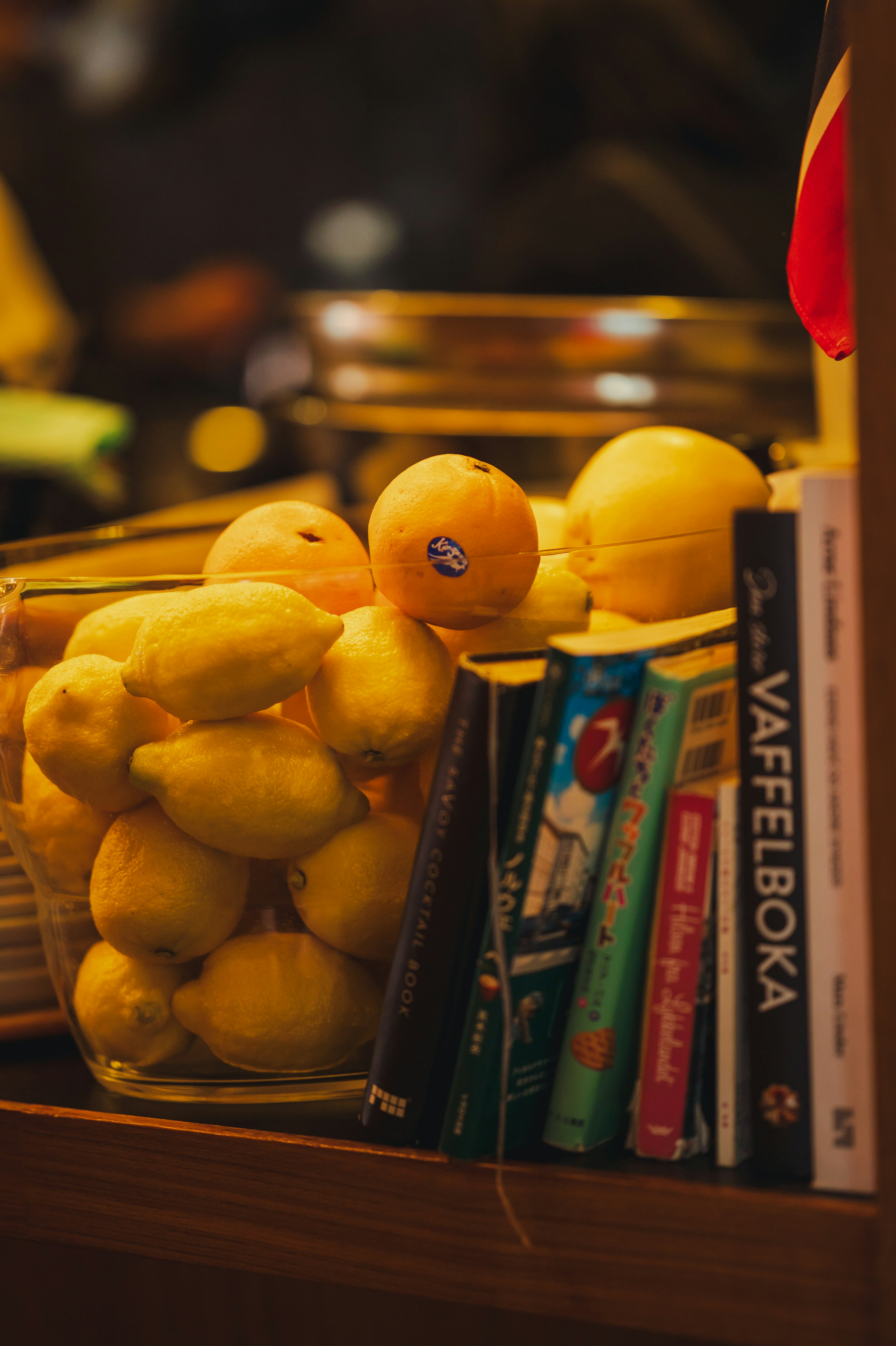 Une étagère avec un bocal en verre rempli de citrons et d'oranges à côté de plusieurs livres