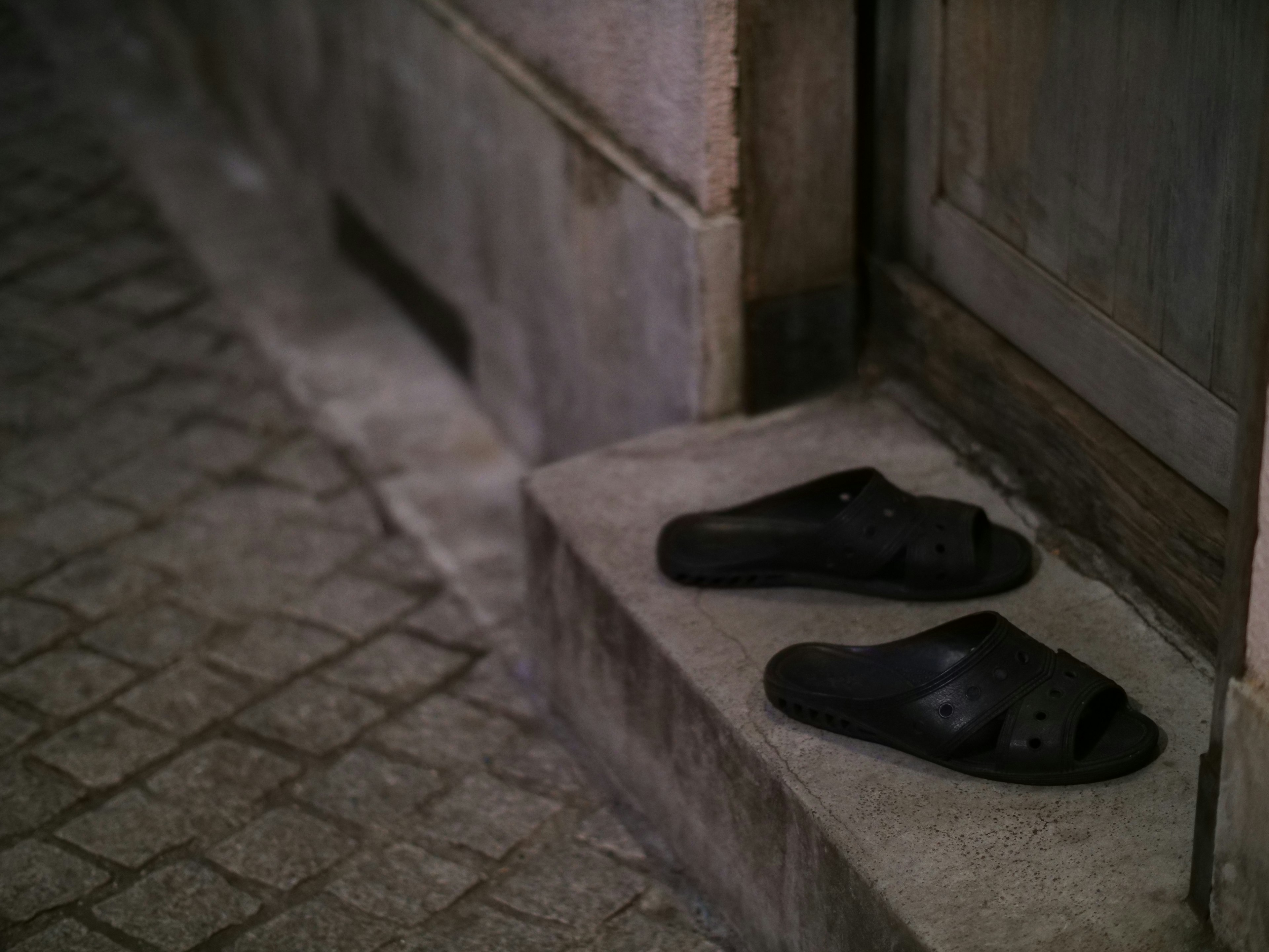 Black sandals placed at the entrance of a door in a nighttime setting