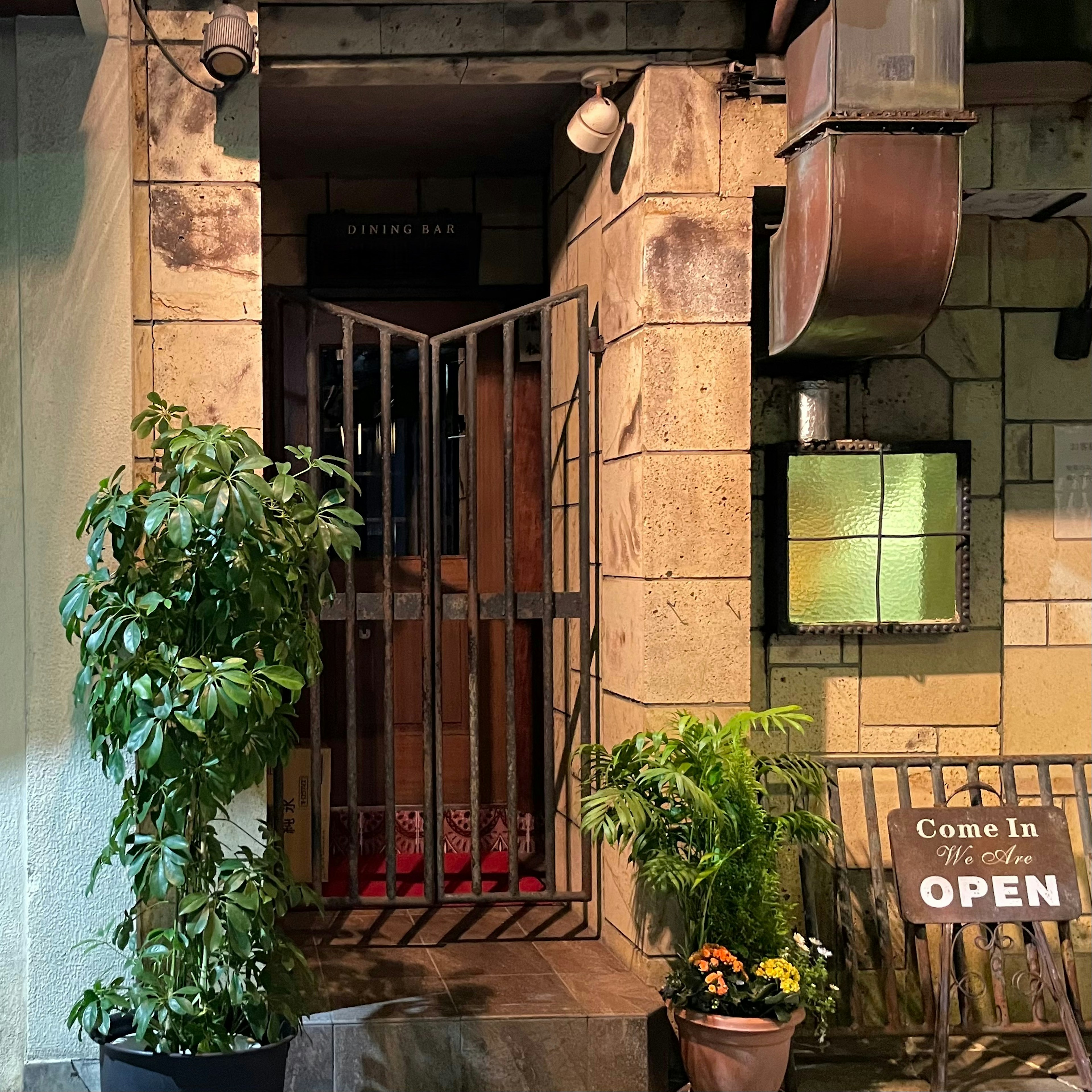 Cafe entrance with stone facade featuring iron gate and green plants