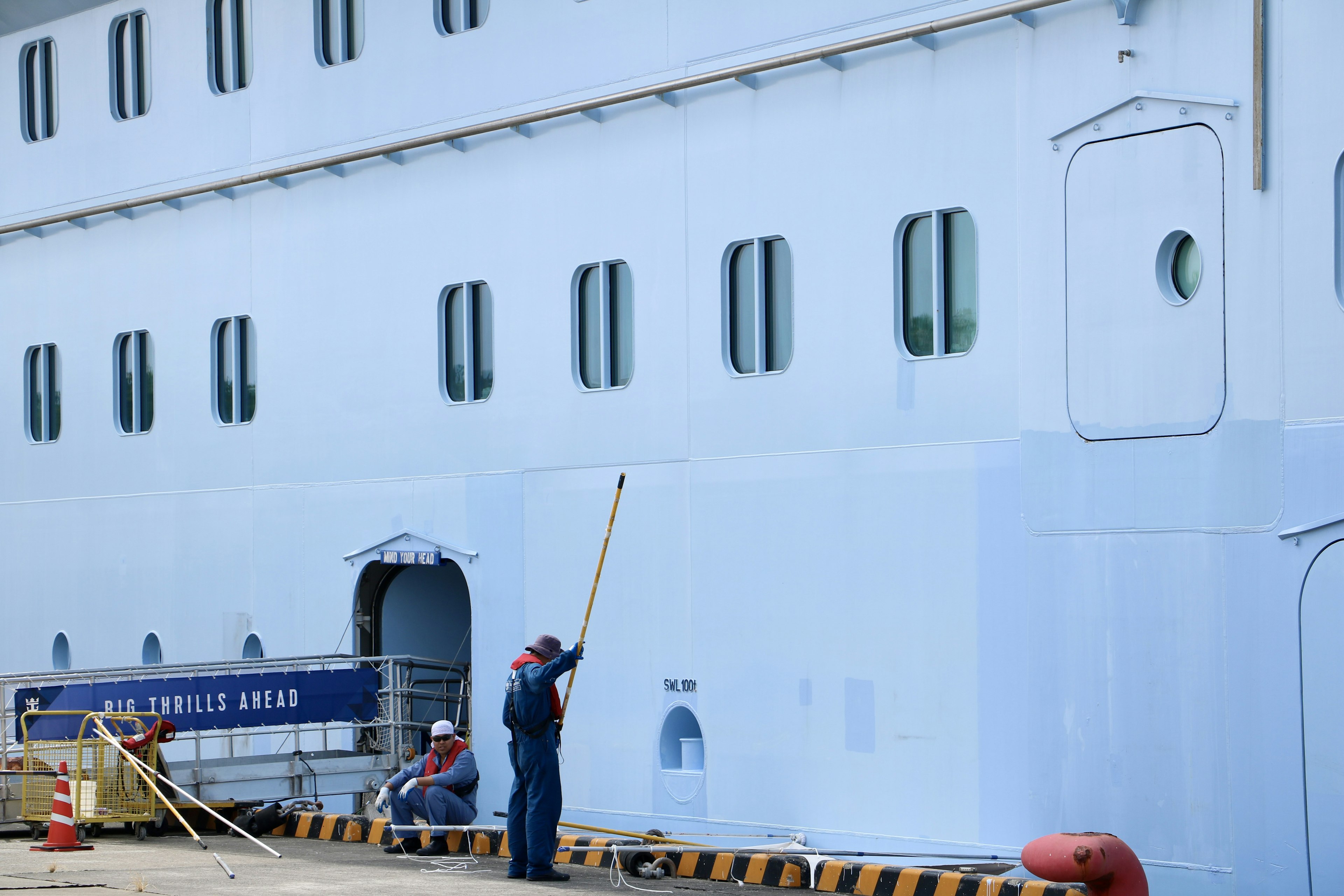 Workers painting the side of a ship