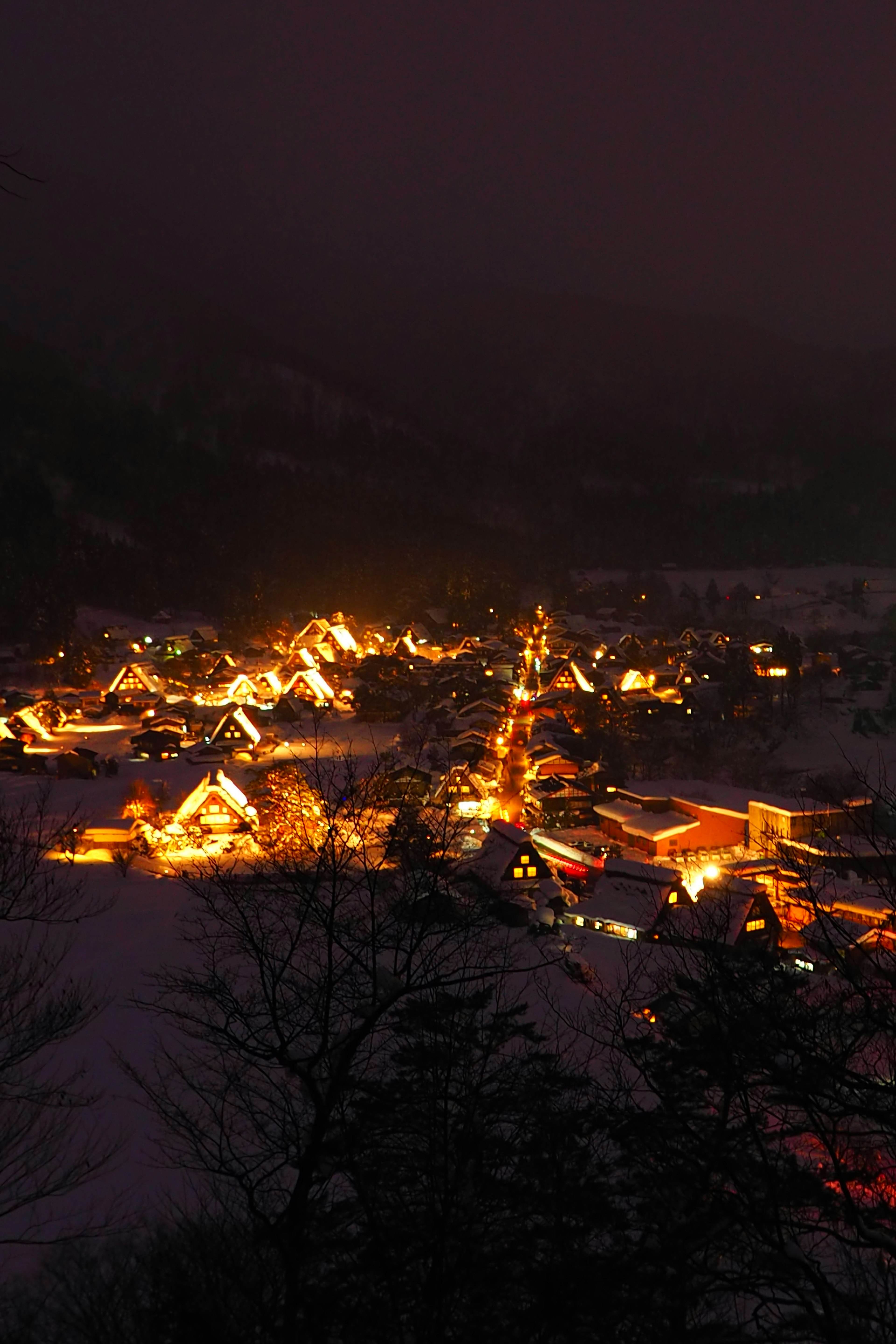 被雪覆盖的村庄夜景，温暖的灯光从房屋中散发，营造宁静的冬季氛围