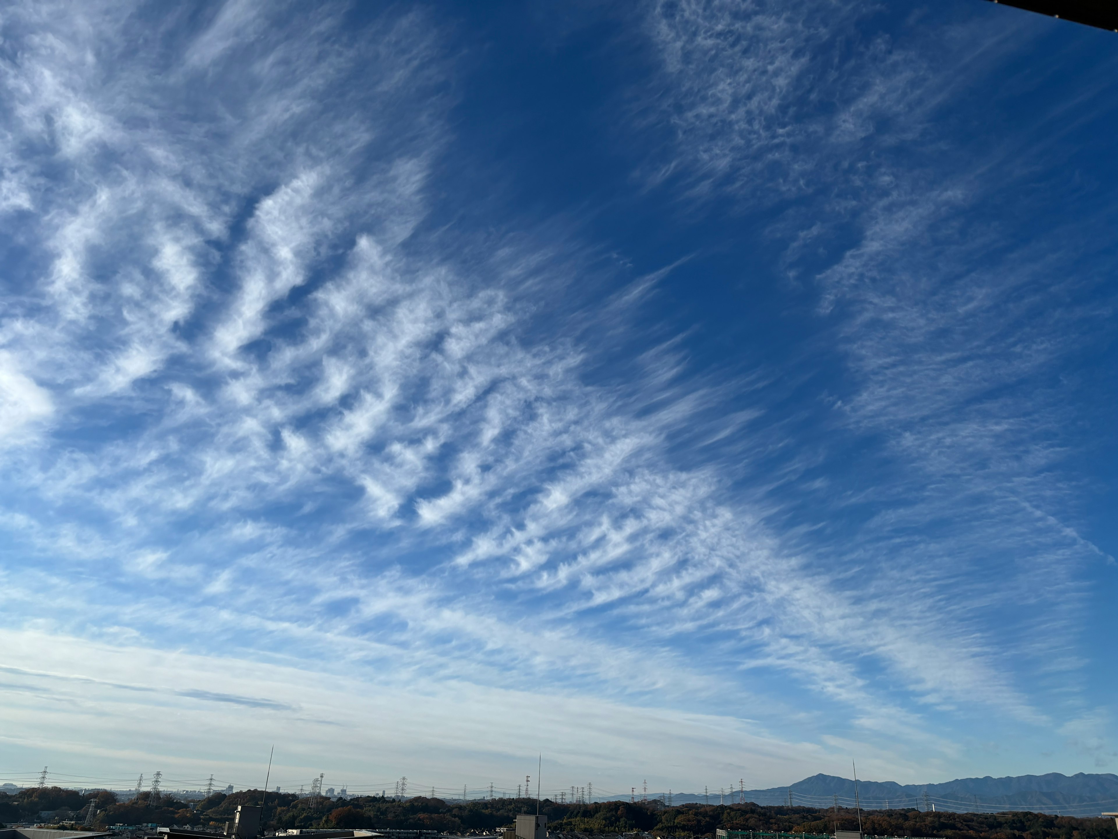 Pemandangan langit biru dengan pola awan mengalir dan gunung di kejauhan