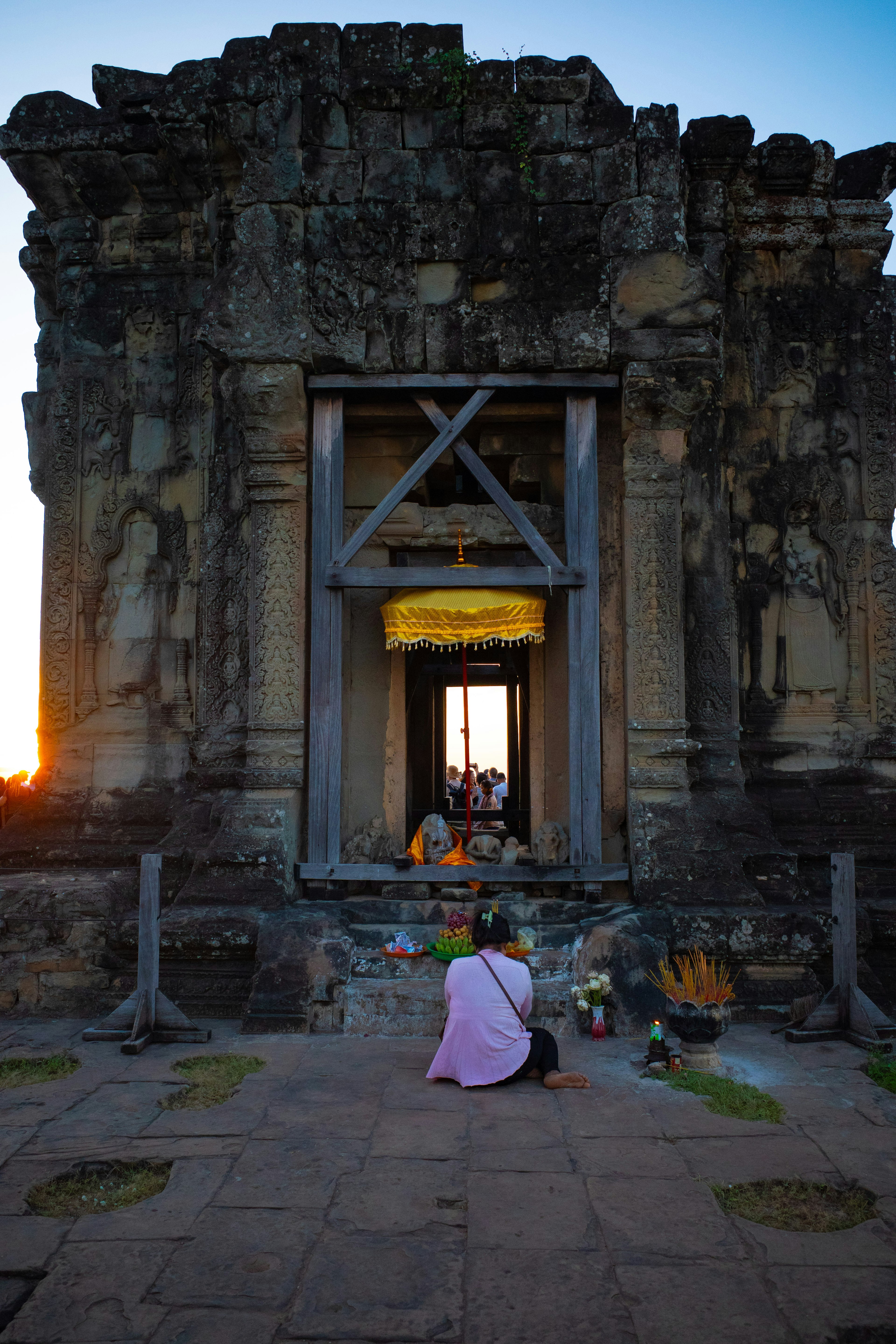 Persona che prega all'ingresso di un antico tempio con il tramonto sullo sfondo