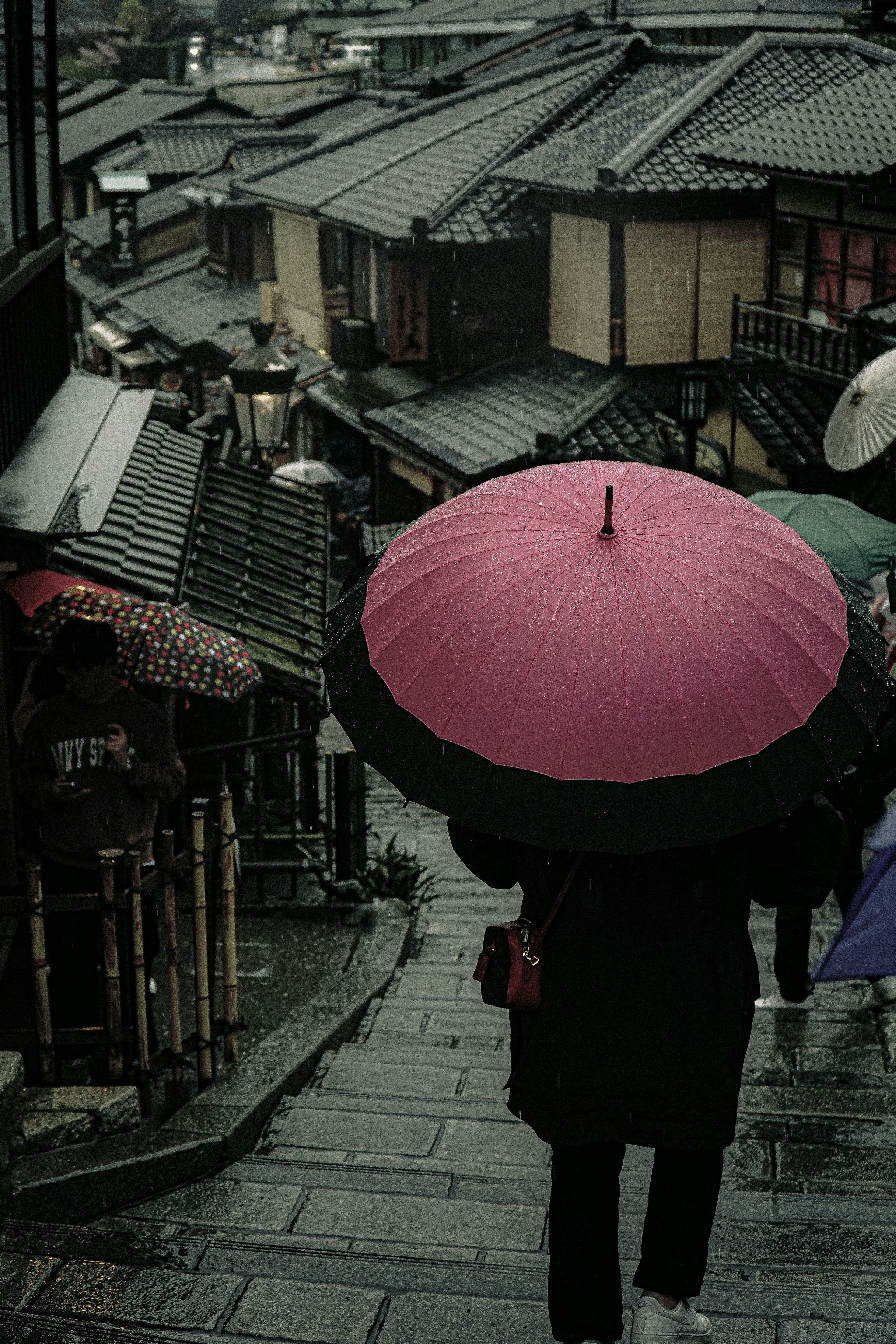 雨の中で大きなピンクの傘を持っている人が古い町並みを歩いている