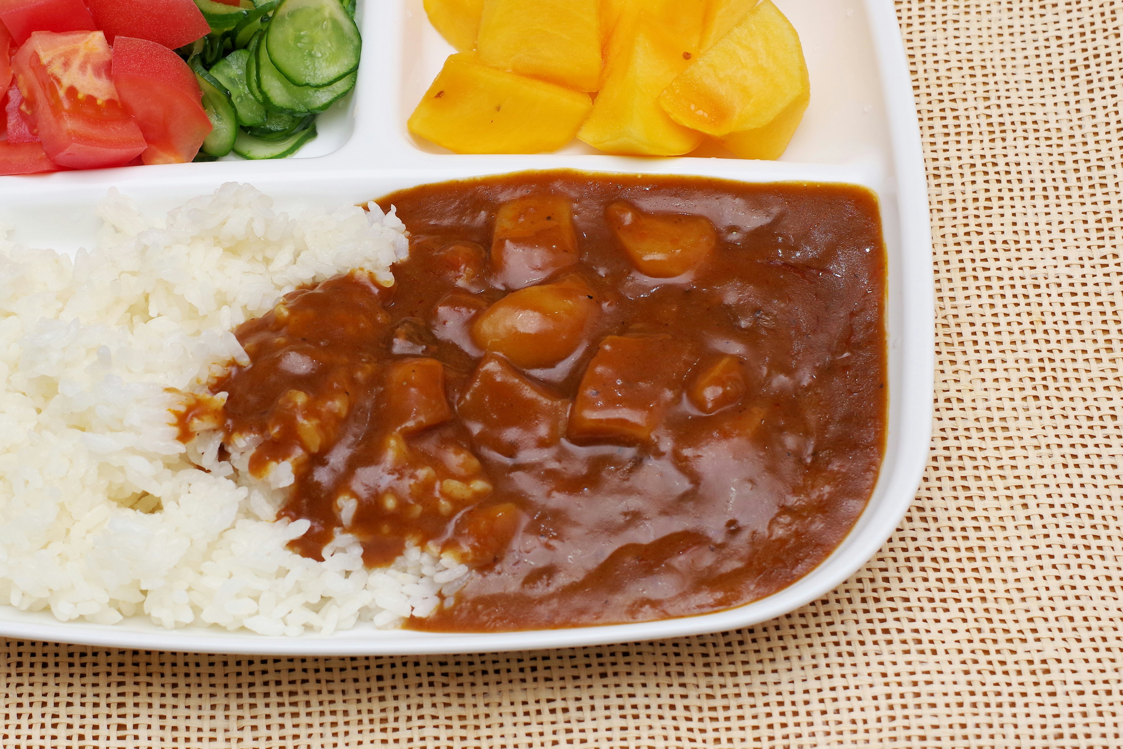 A meal plate featuring white rice and curry sauce with diced vegetables