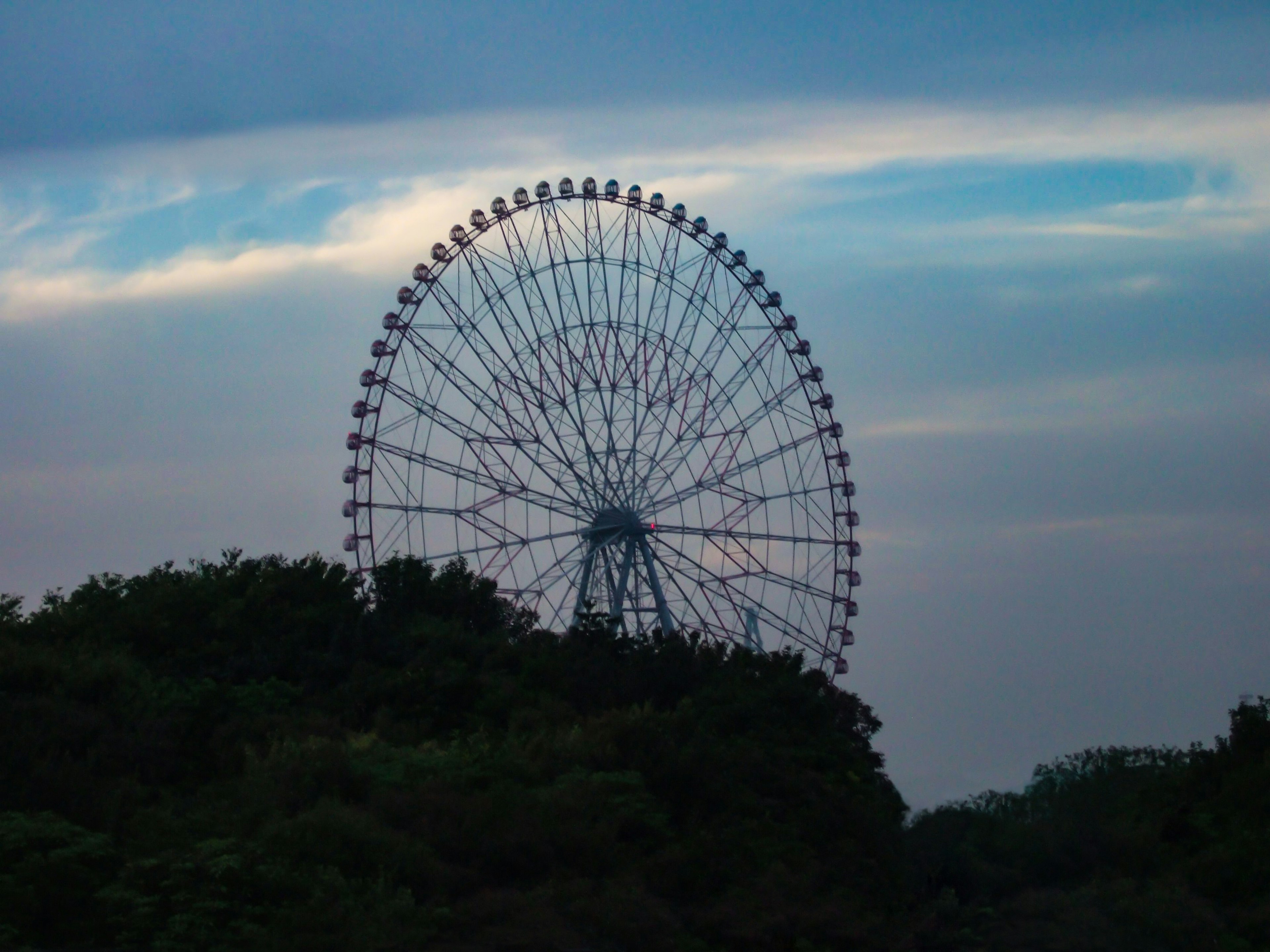 Ferris wheel silhouette against a blue sky with clouds