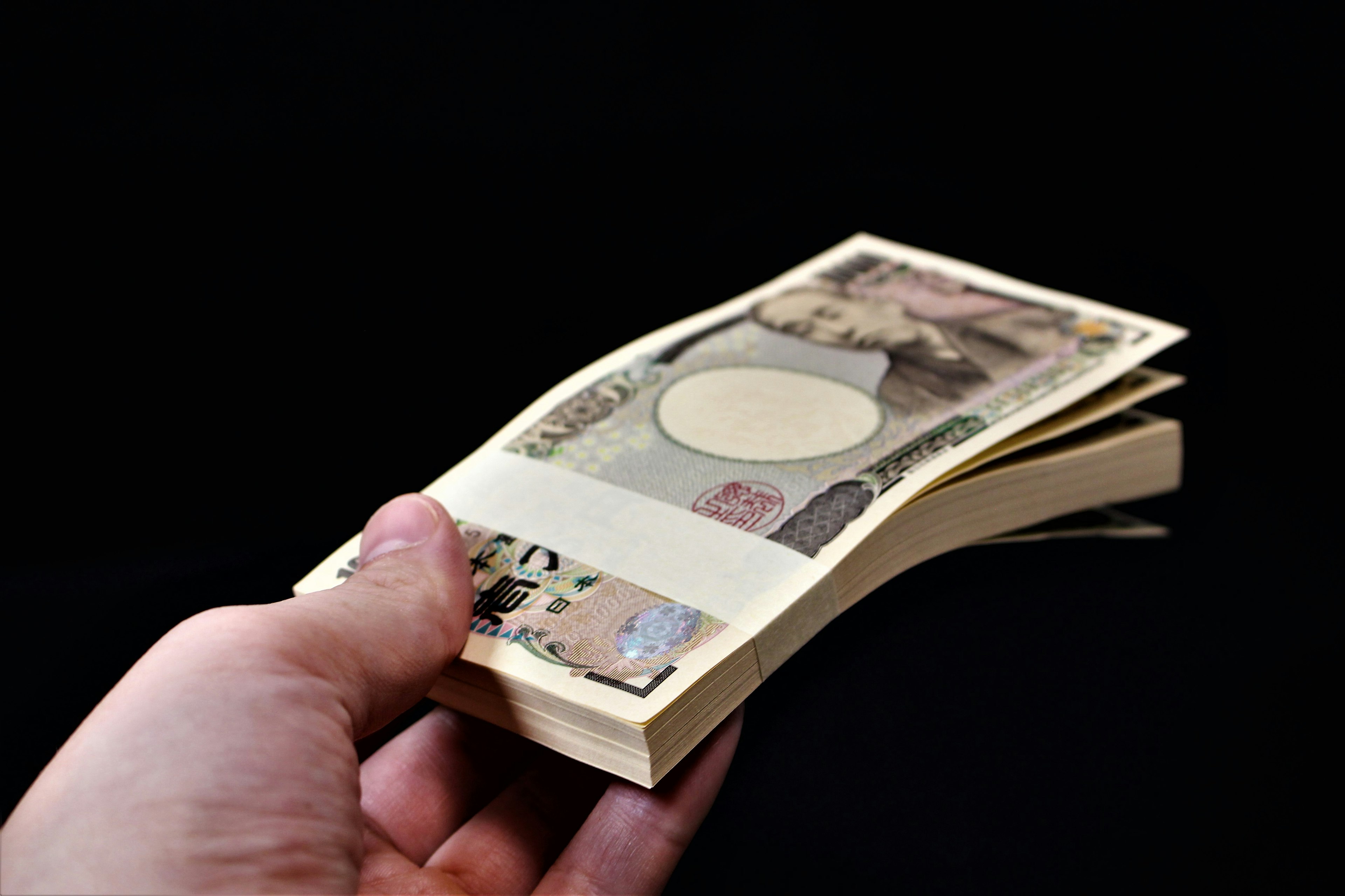 Une main tenant une liasse de billets japonais sur un fond noir