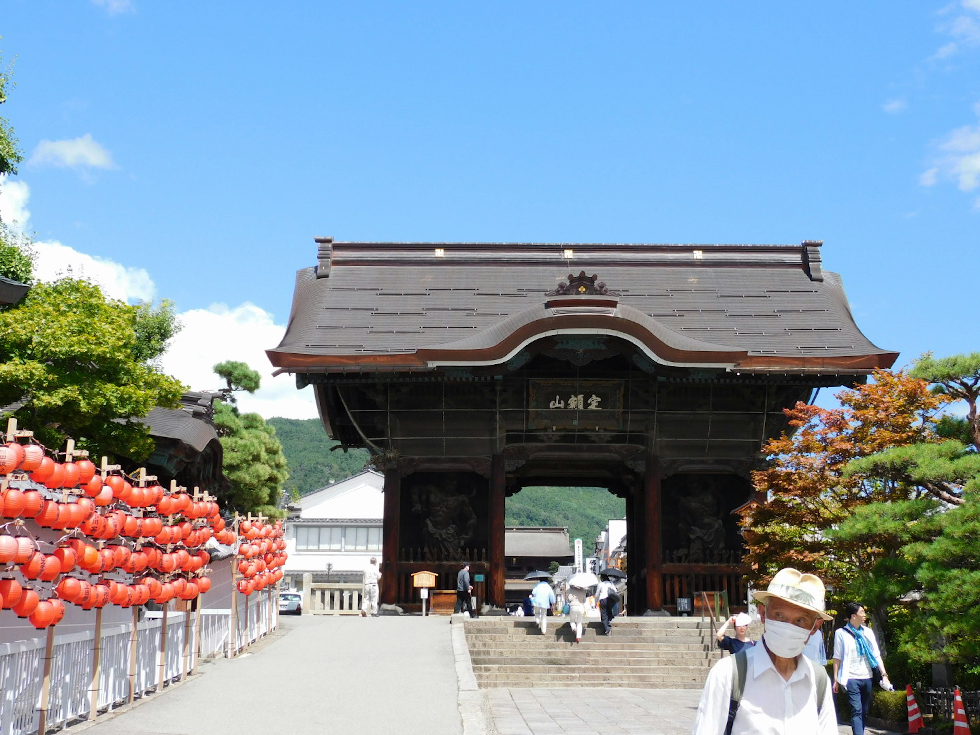 Traditionelles japanisches Tor unter blauem Himmel mit roten Laternen entlang des Weges