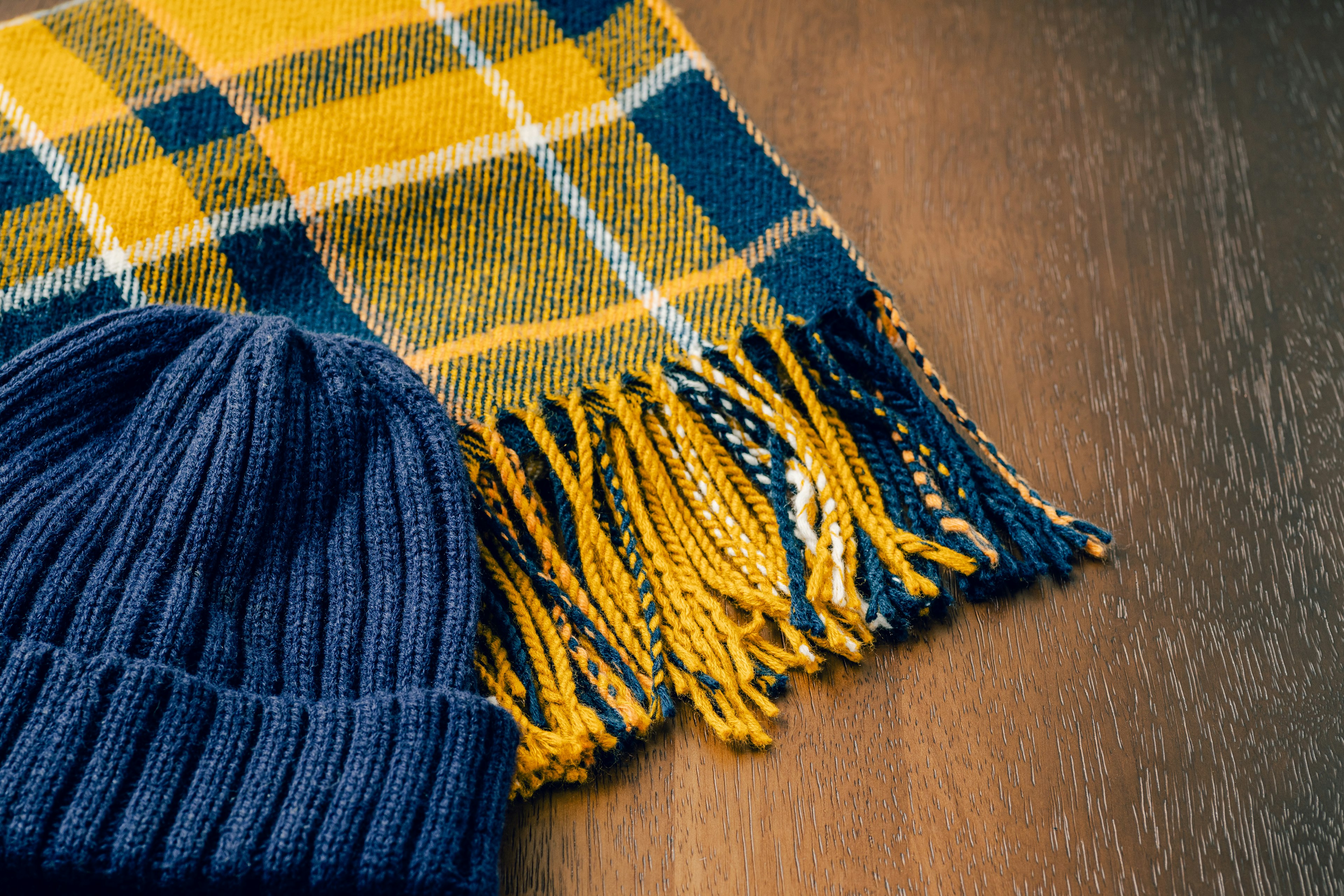 Une écharpe à carreaux jaune et bleu et un bonnet en tricot bleu marine sont posés sur une table en bois