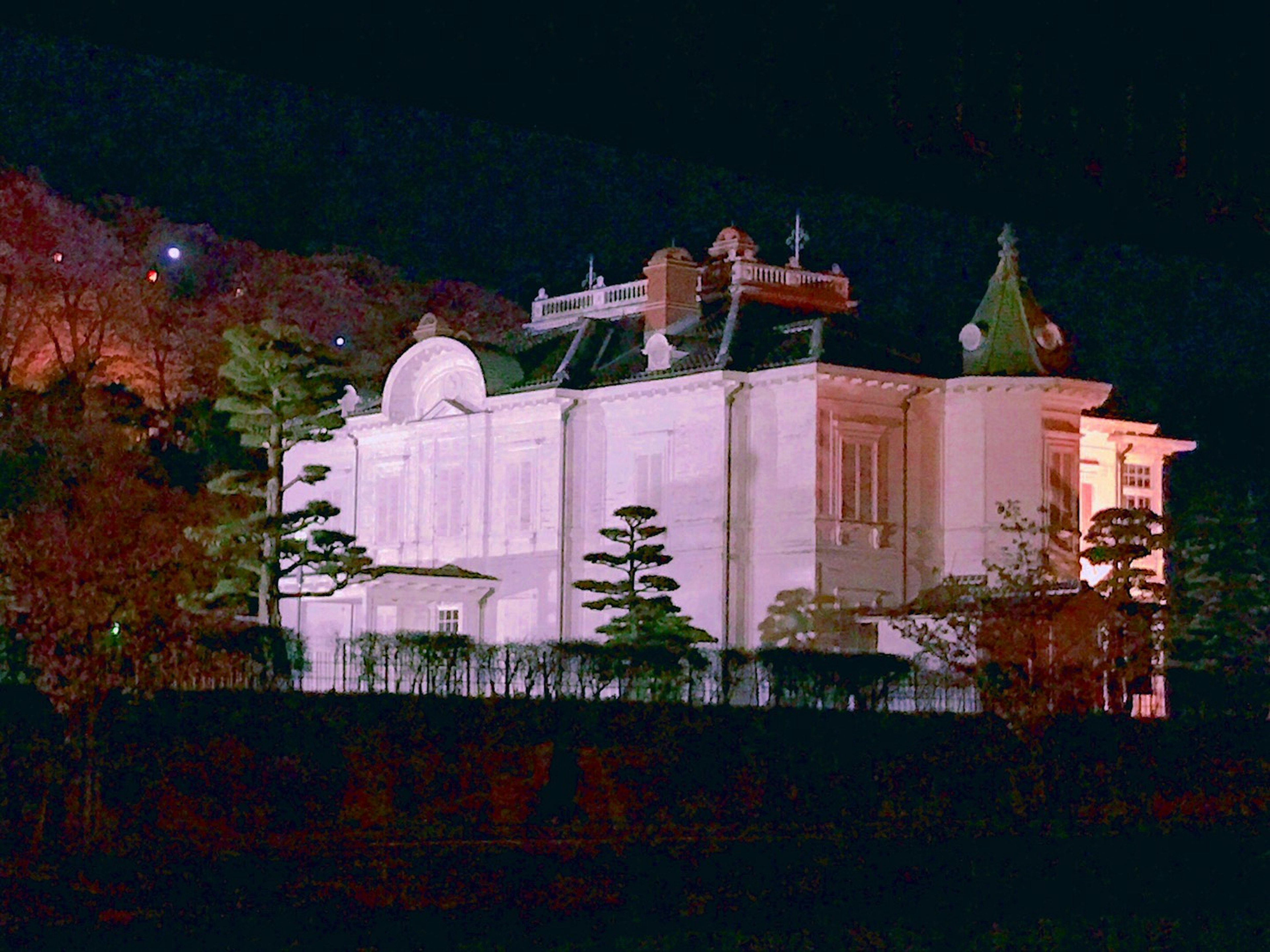 Beautiful white mansion at night featuring intricate details and green roofs