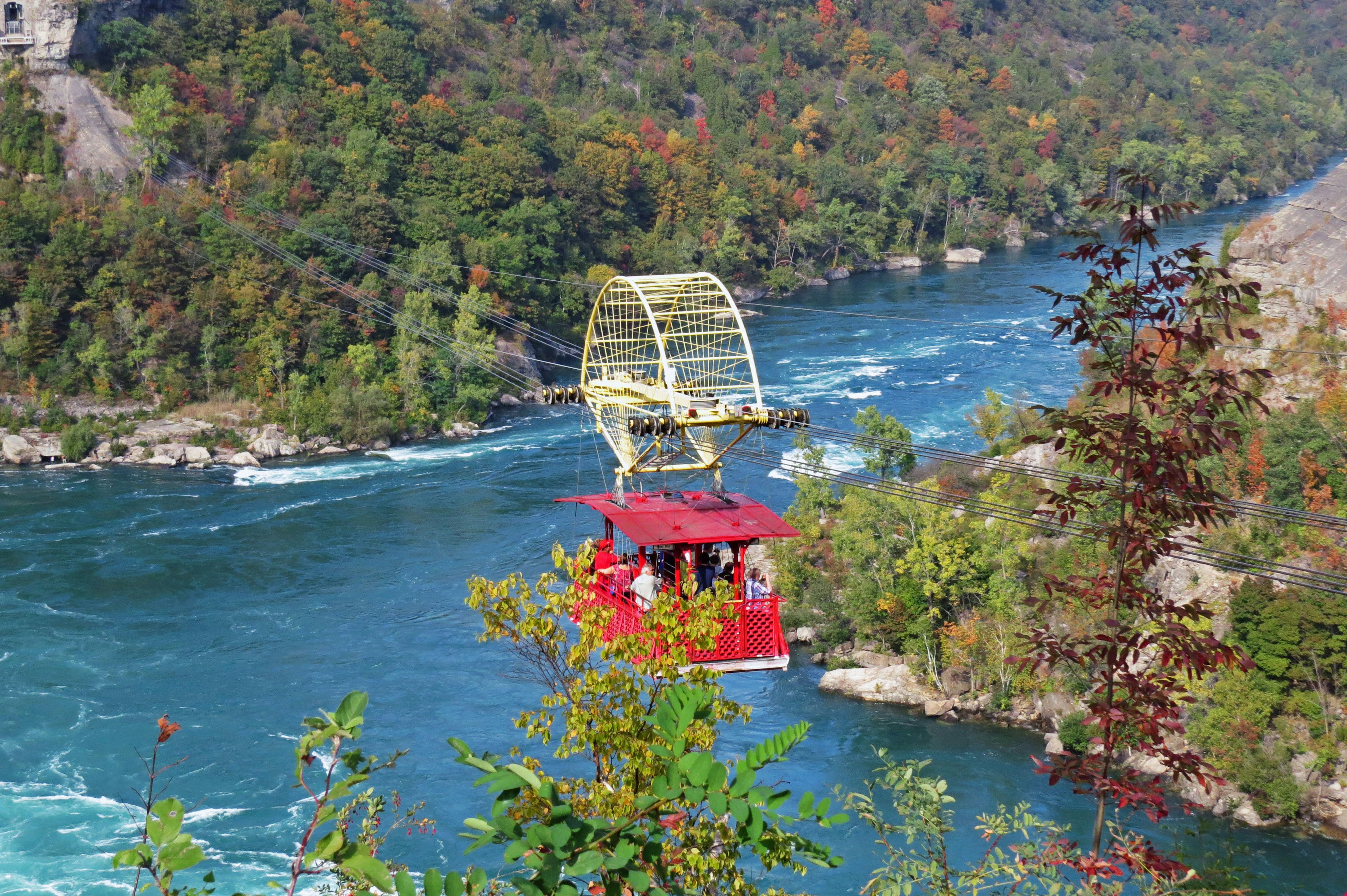 Teleférico rojo cruzando un río con follaje otoñal vibrante