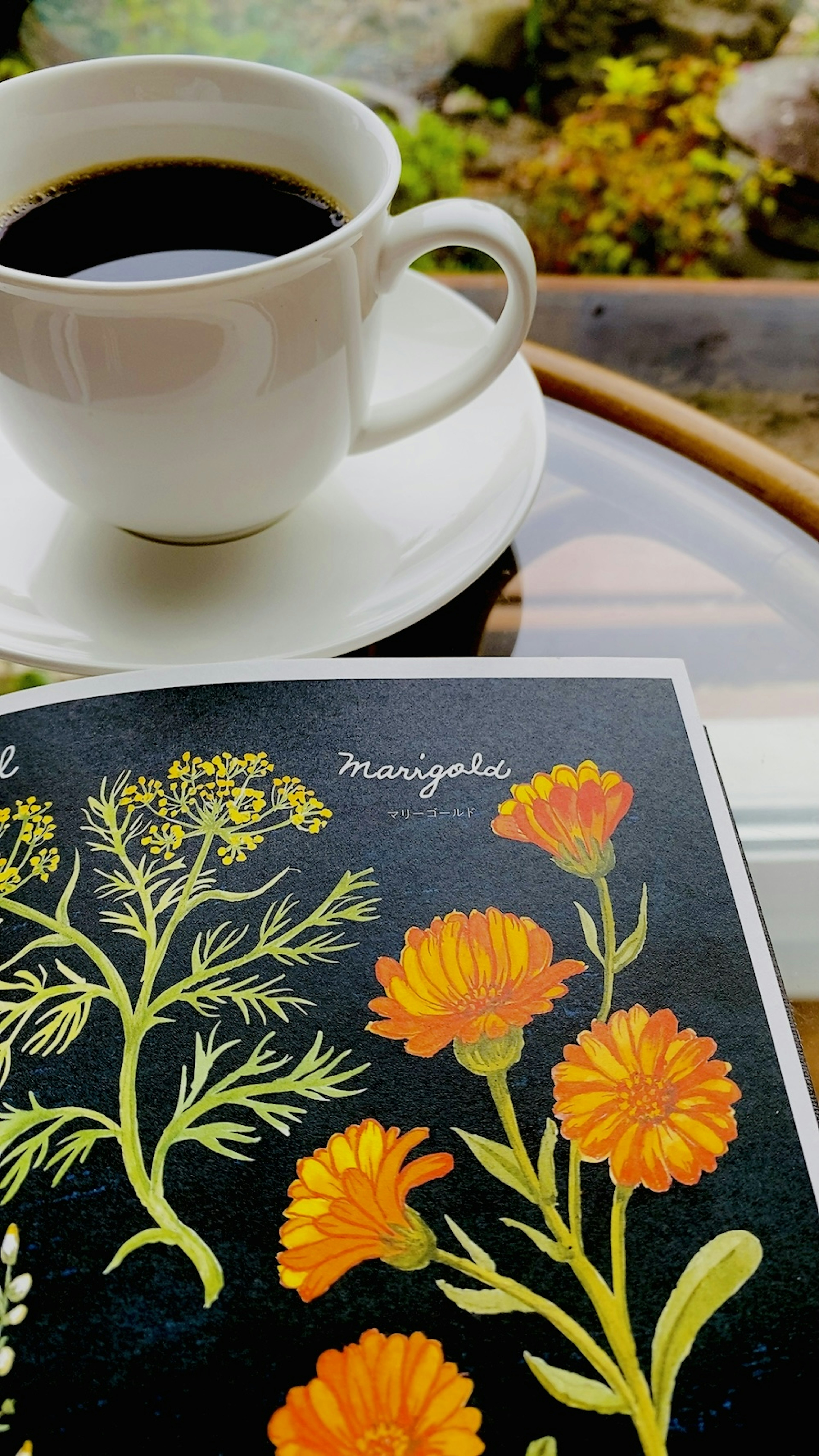 Una taza de café negro al lado de un libro con flores naranjas sobre fondo negro