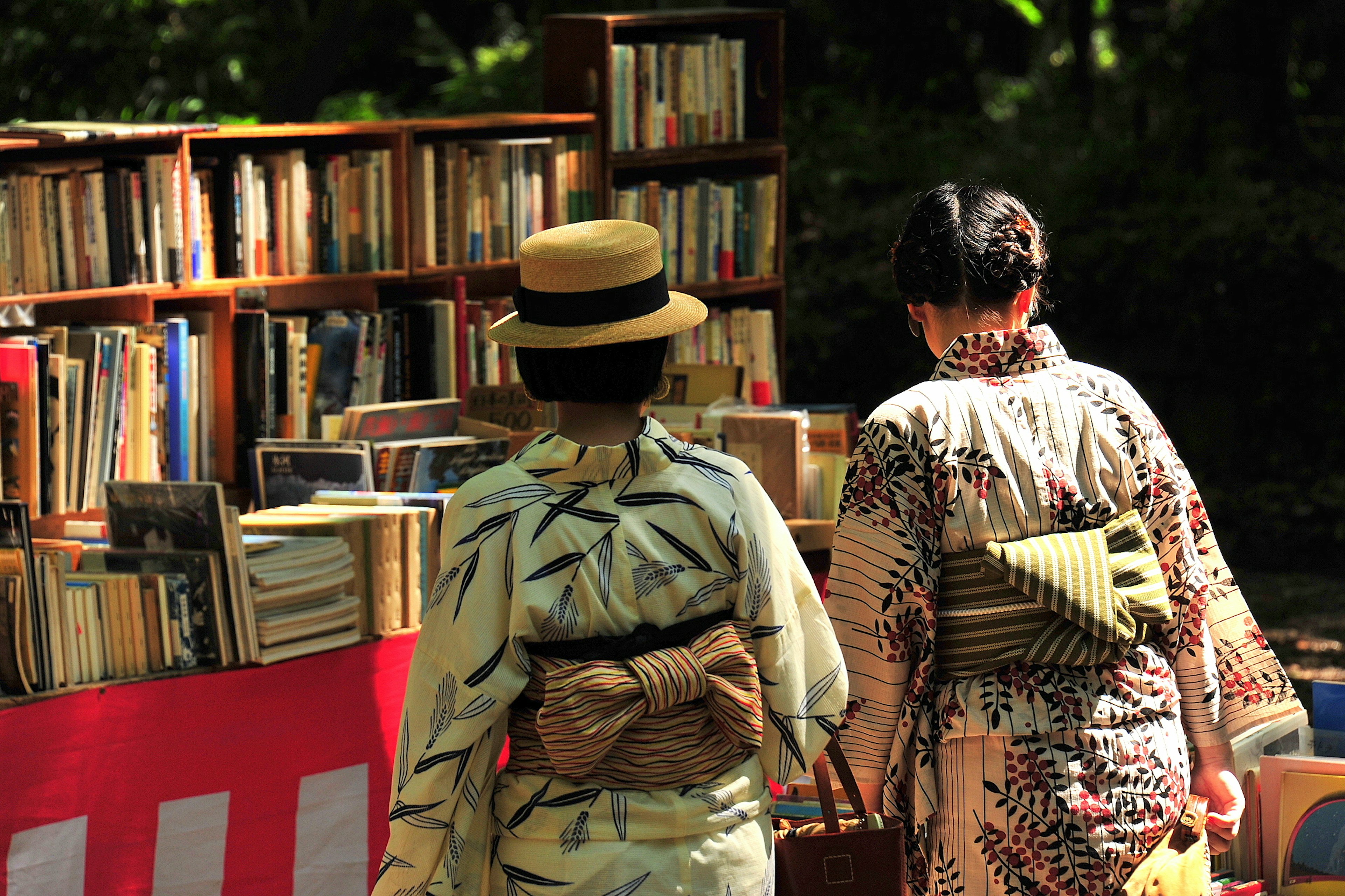 Dua wanita berjalan di depan stan buku mengenakan kimono tradisional banyak buku ditampilkan